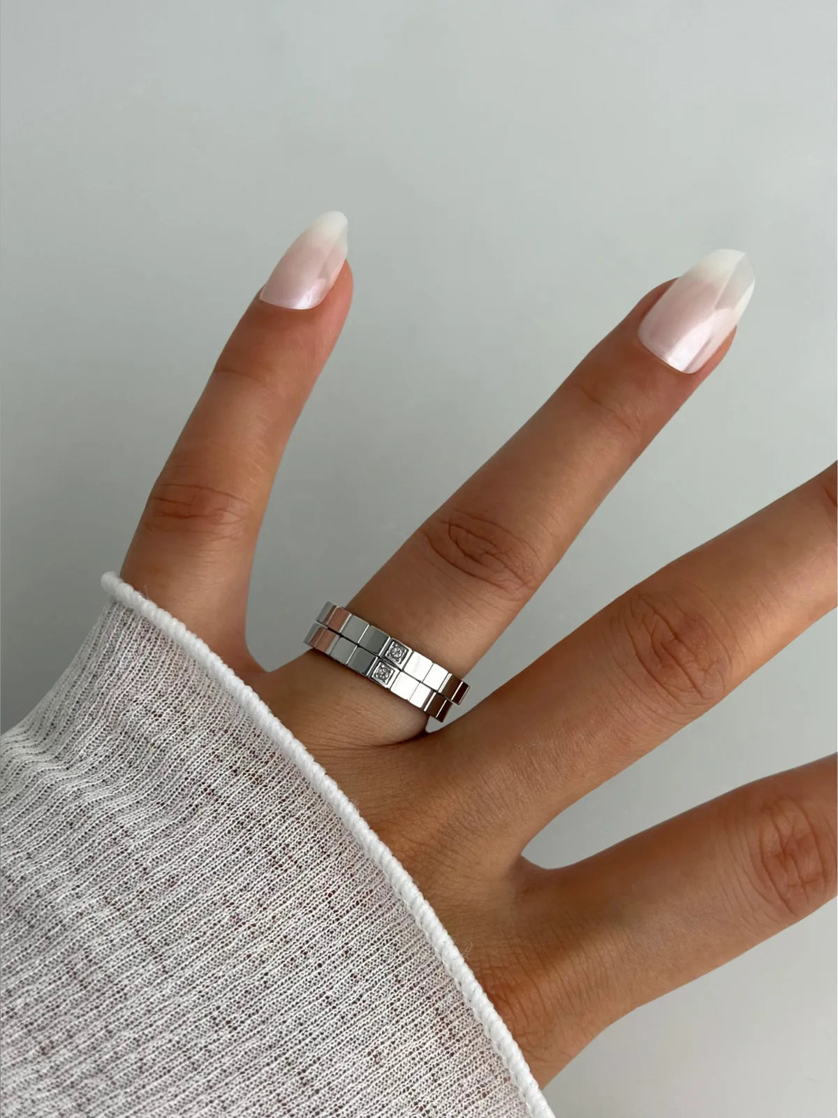 Celina RING-Hand wearing a silver ring with a light gray sleeve on a neutral background