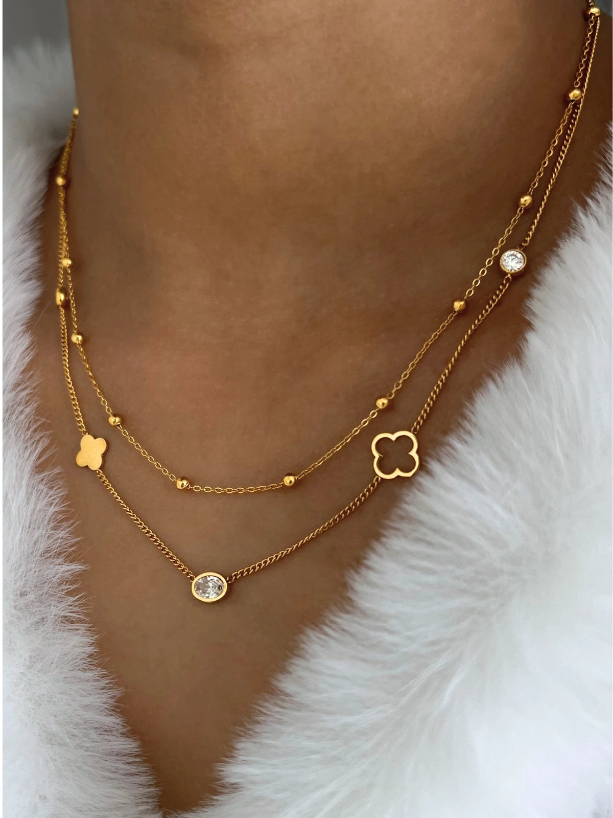 Clover Blossom Necklace – On Model Styled Shot-Gold necklaces with floral and round pendants on a person wearing a white fur garment.