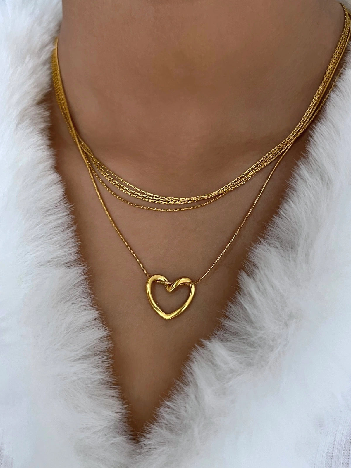 Darla Heart Necklace – On Model Styled Shot. Gold heart-shaped necklace on a person against a white fur background