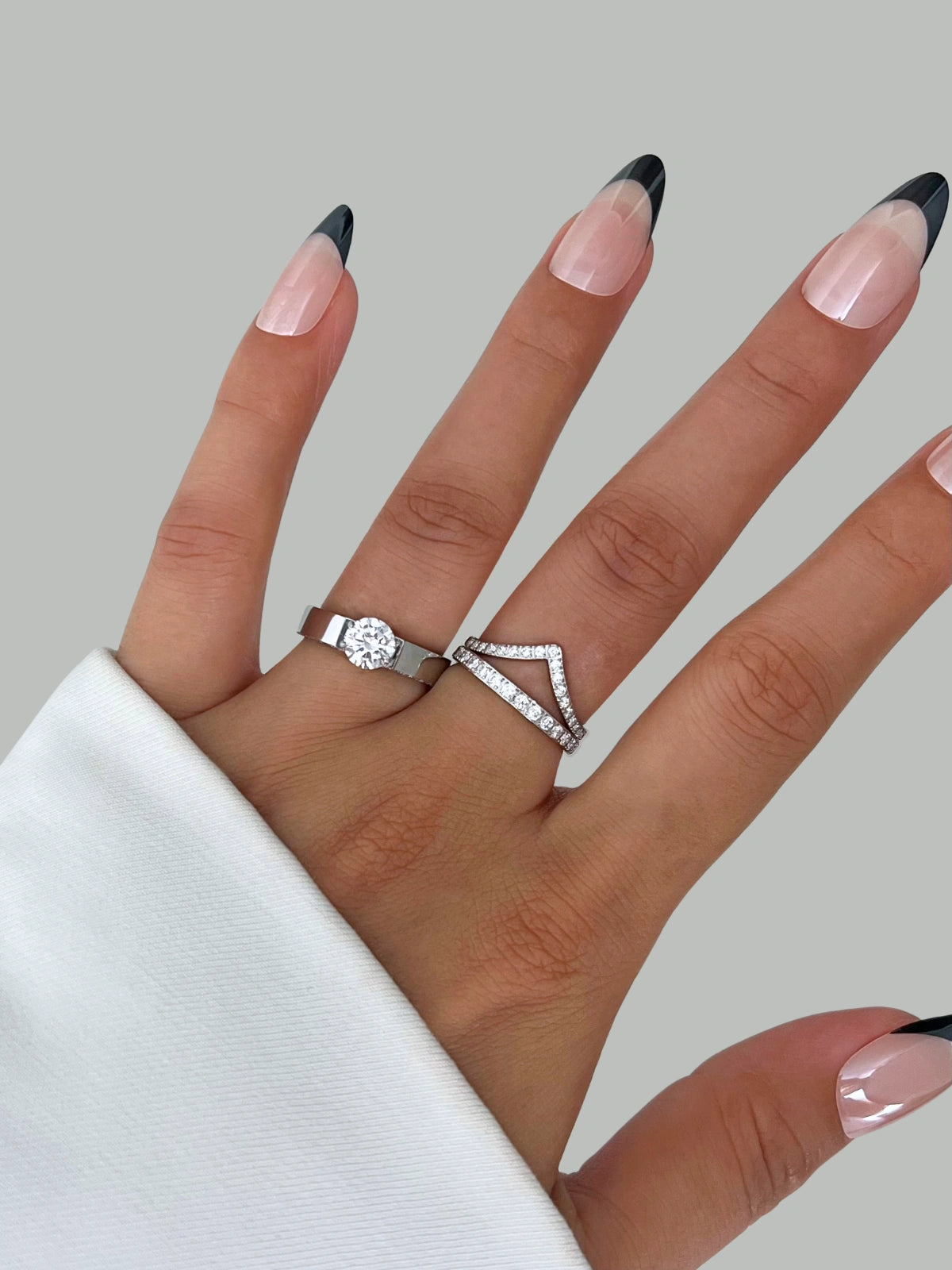 Dolores Ring – Worn on Finger-Hand wearing two silver rings with a plain background