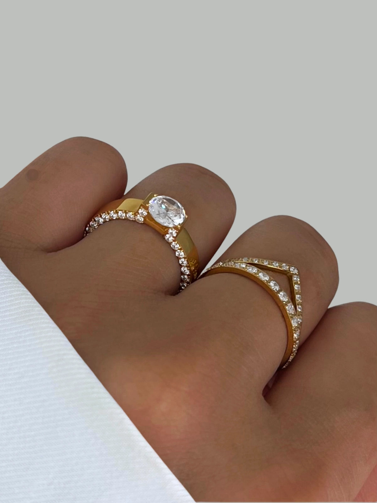 Dolores Ring – Worn on Finger-Gold ring with a clear gemstone on a finger against a light background