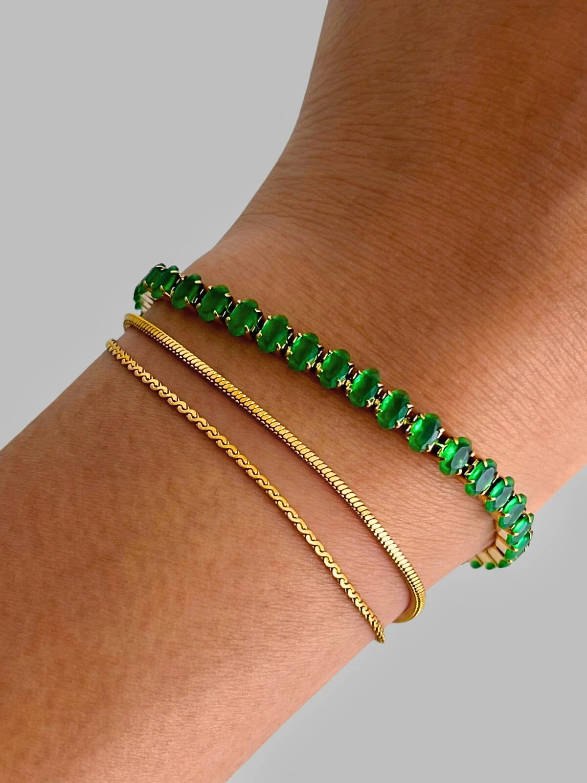 Dua Layered Bracelet – Close-Up Detail-Green beaded bracelet and gold chain bracelet on a wrist against a gray background