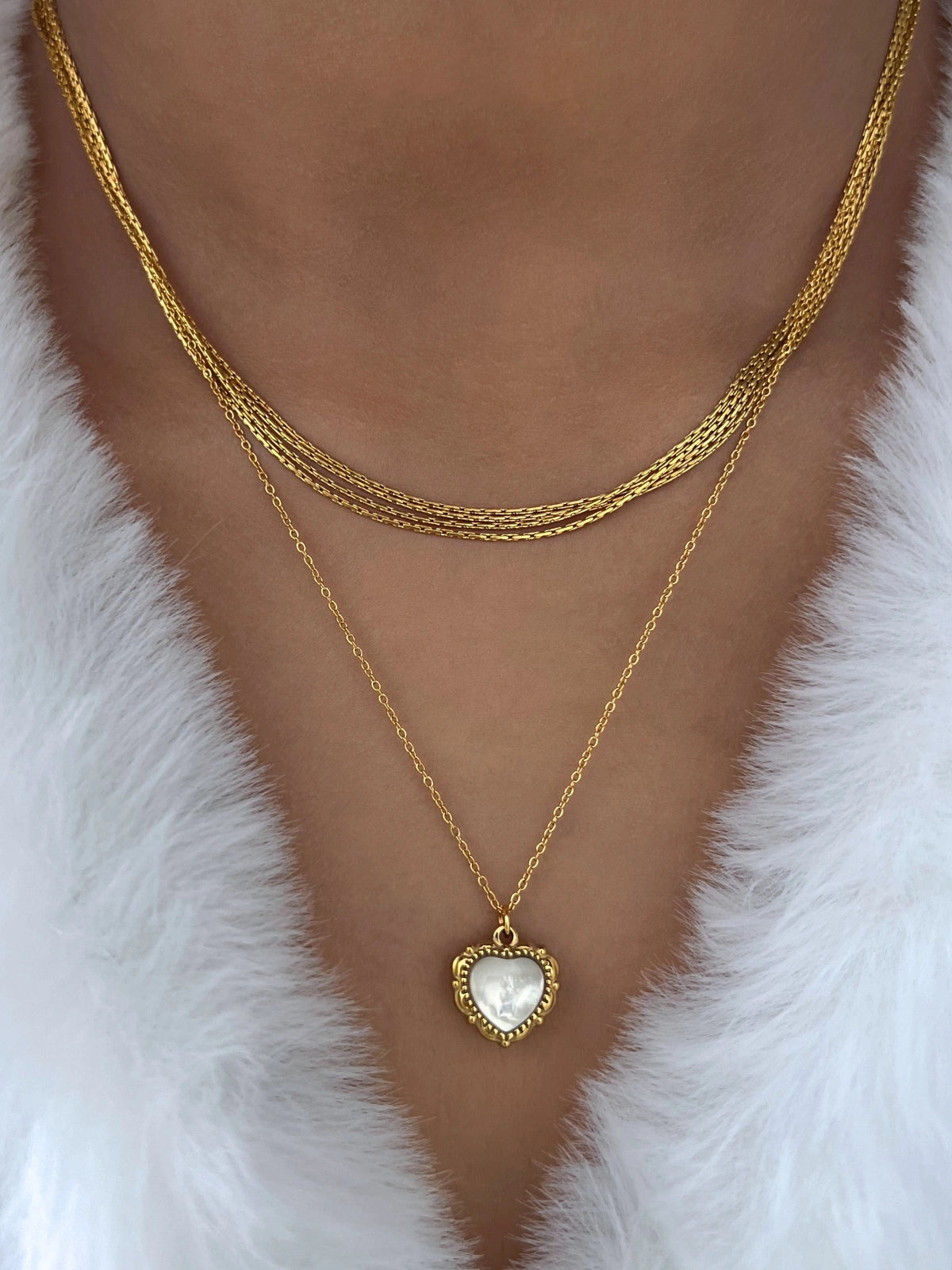 Elizelle Chain – On Model Styled Shot-Gold necklace with a heart-shaped pendant on a white fur background