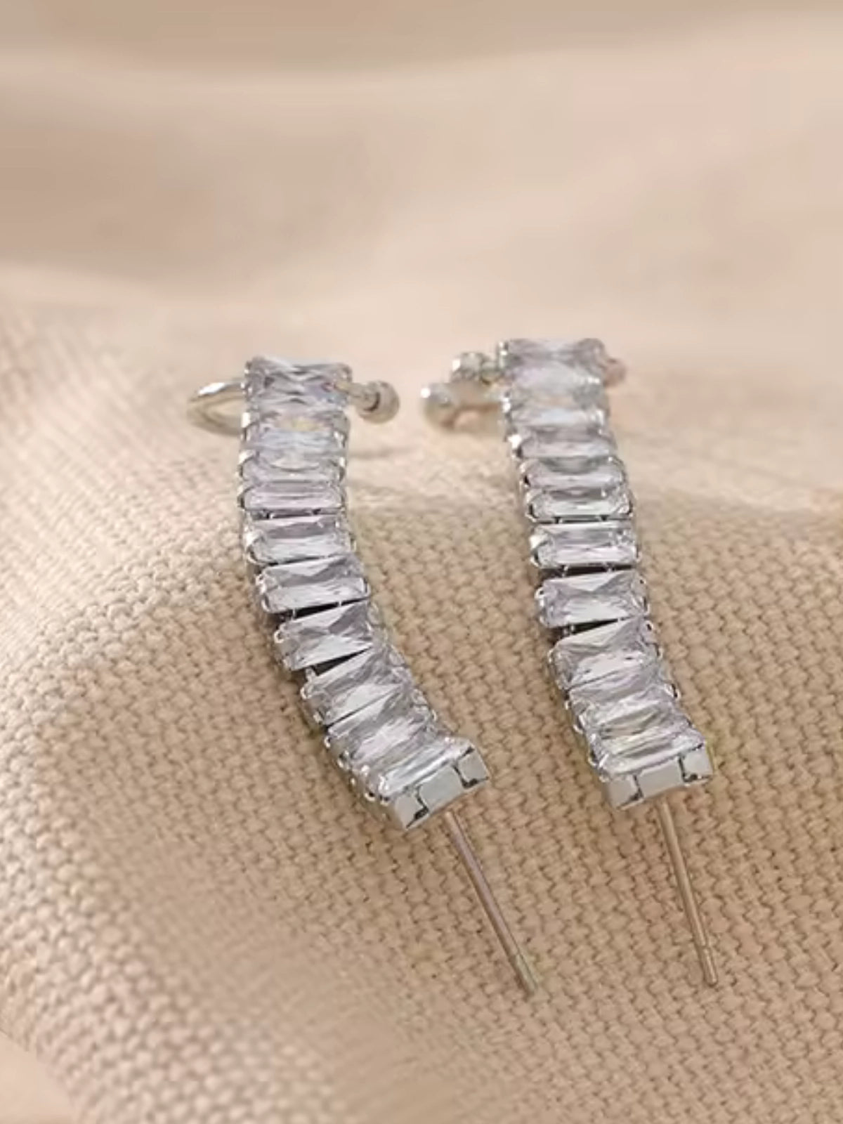 Elly_Earring_Cuff_Close_Up_Detail-Gold-Pair of silver hoop earrings on a beige fabric background