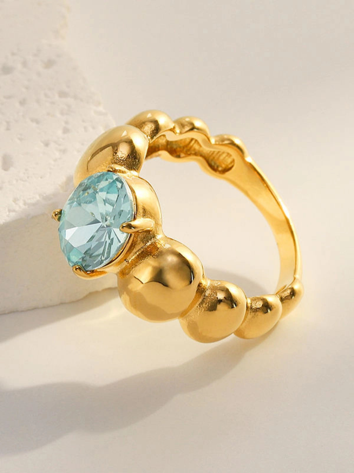 Fabiana_Ring_Front_VieW Gold ring with a blue gemstone on a light background