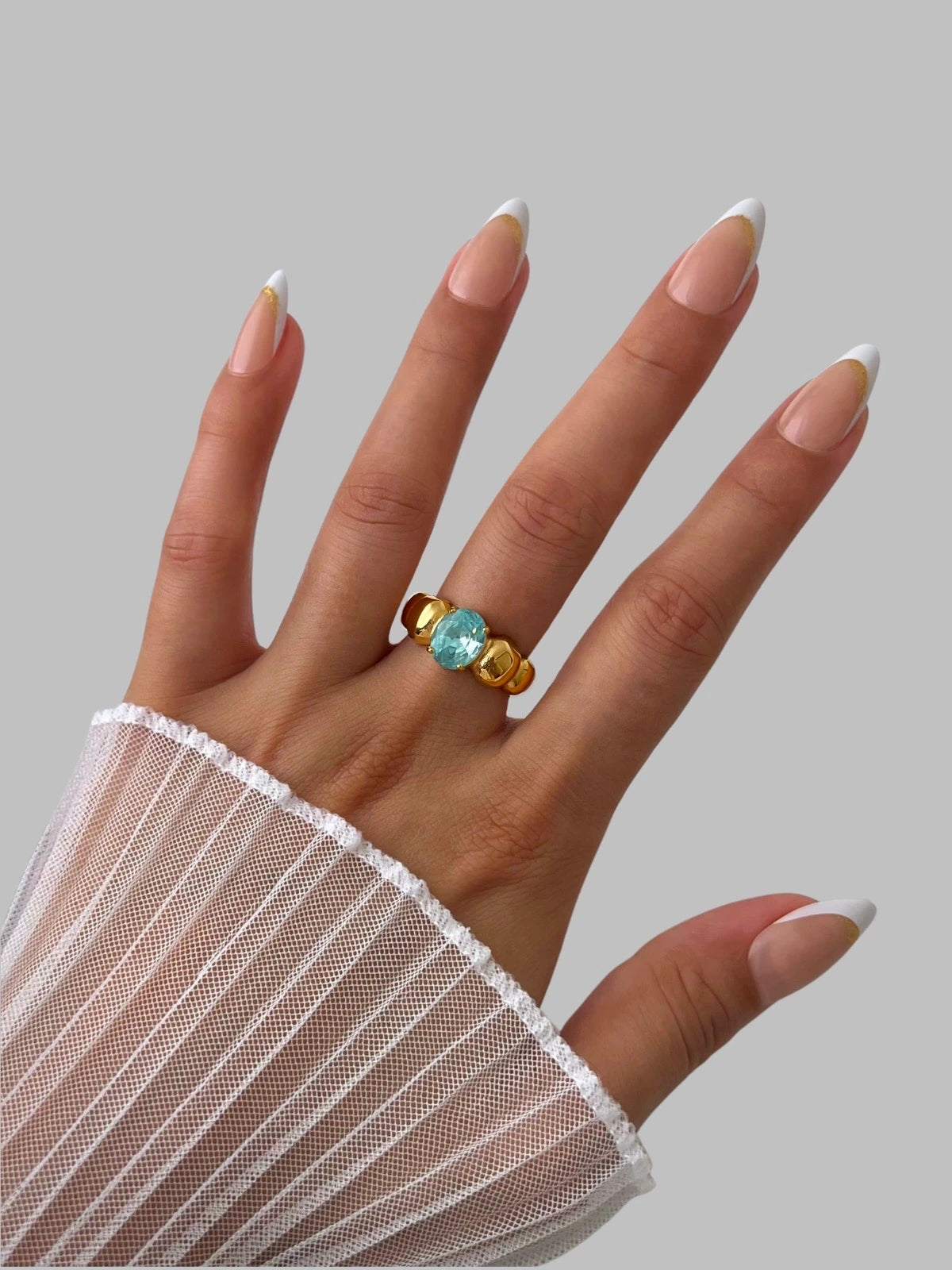 Fabiana Ring – Worn on Finger-Hand wearing a gold ring with a blue gemstone on a gray background