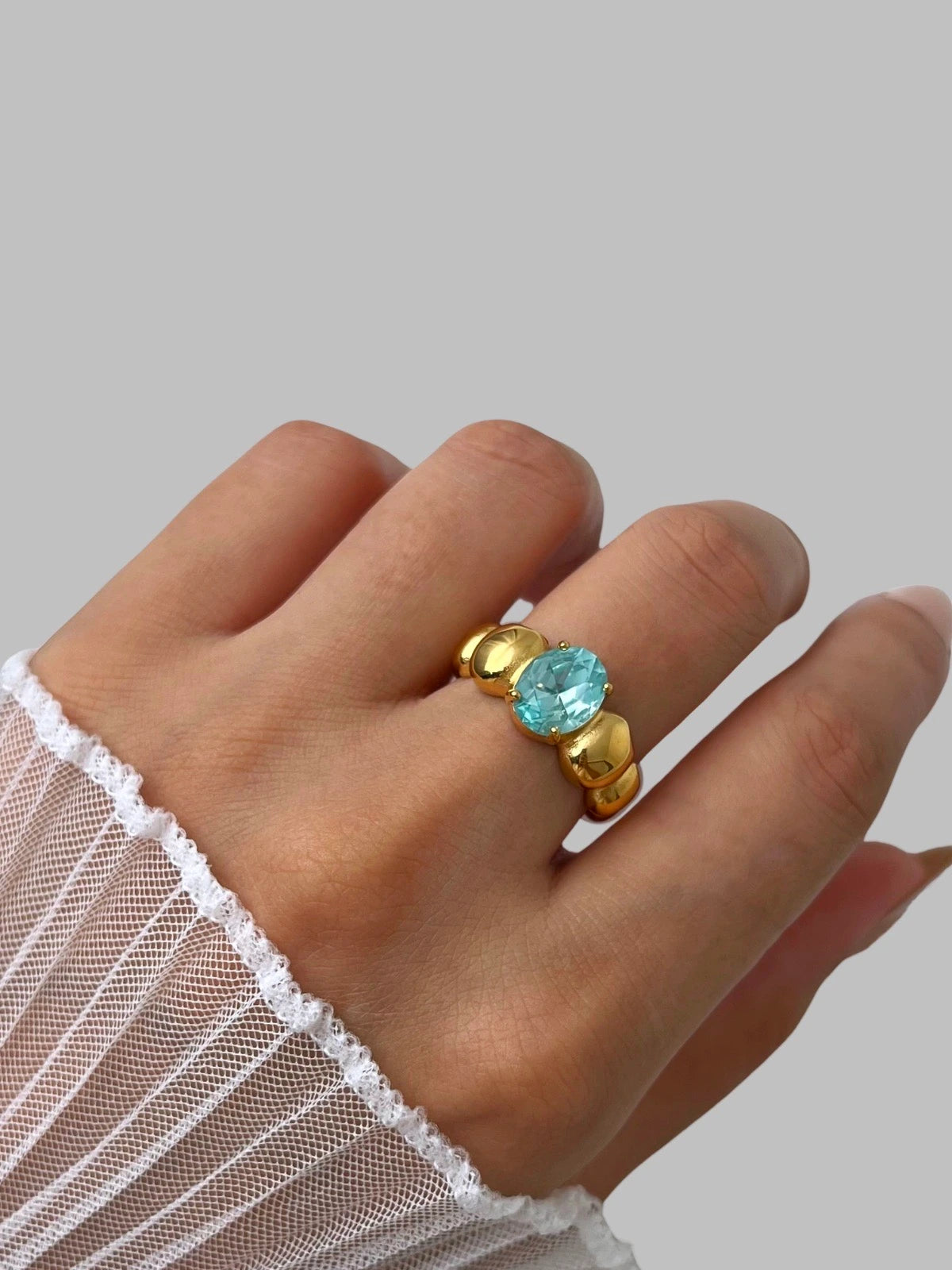 Fabiana Ring – Worn on Finger-Hand wearing a gold ring with a blue gemstone on a plain background
