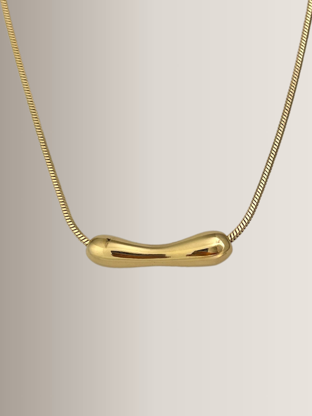 Halia Necklace – Close‑Up Detail-Gold necklace with a unique pendant on a light beige background