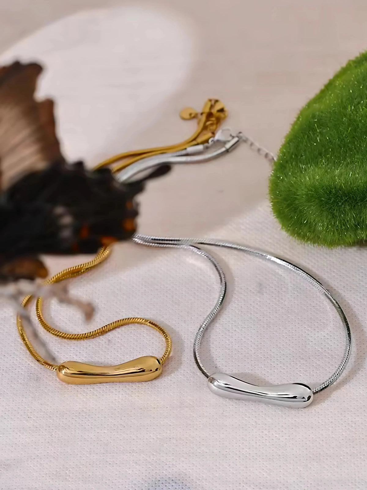 Halia Necklace – Close‑Up Detail-Gold and silver bangles on a textured surface with a butterfly and green leaf.