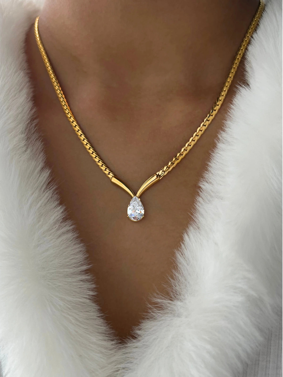 Imber Necklace – On Model Styled Shot-Gold necklace with a teardrop-shaped pendant worn by a person in a white fur garment.