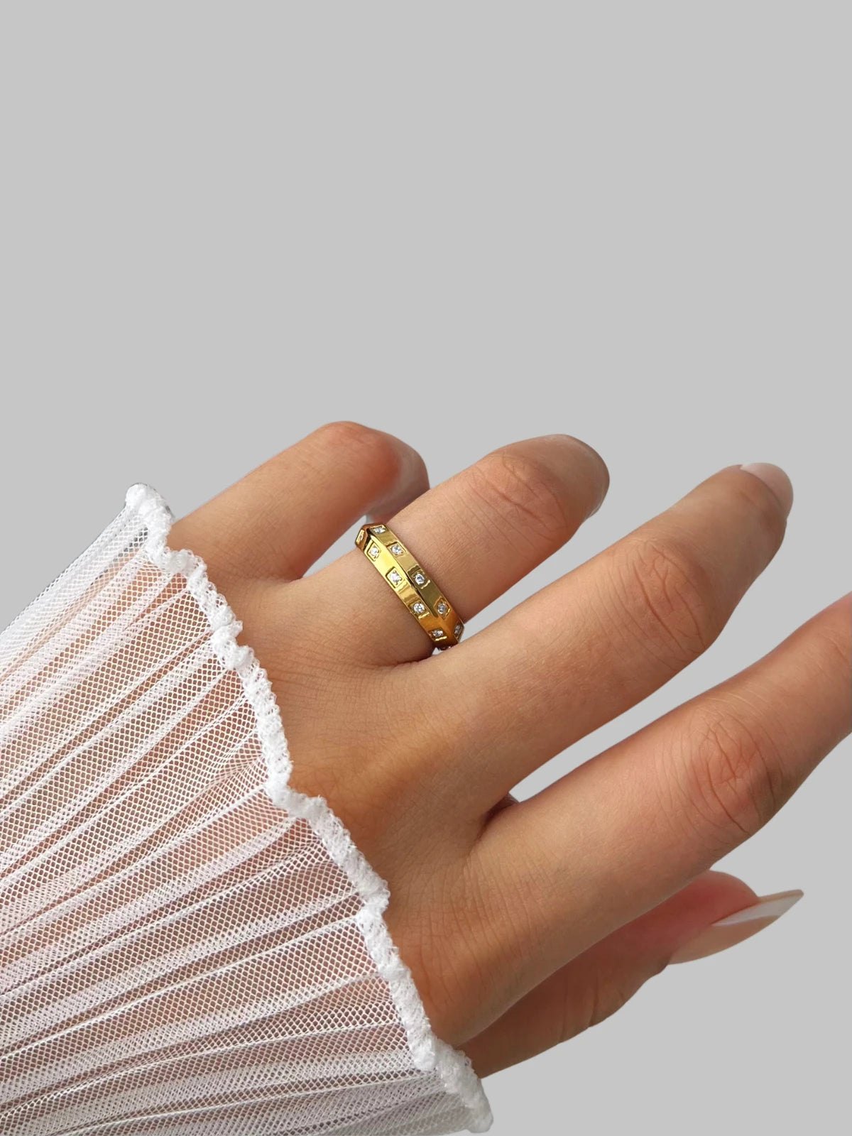 Lucena Ring – Worn on Finger-Hand wearing a gold ring with a white sleeve on a gray background