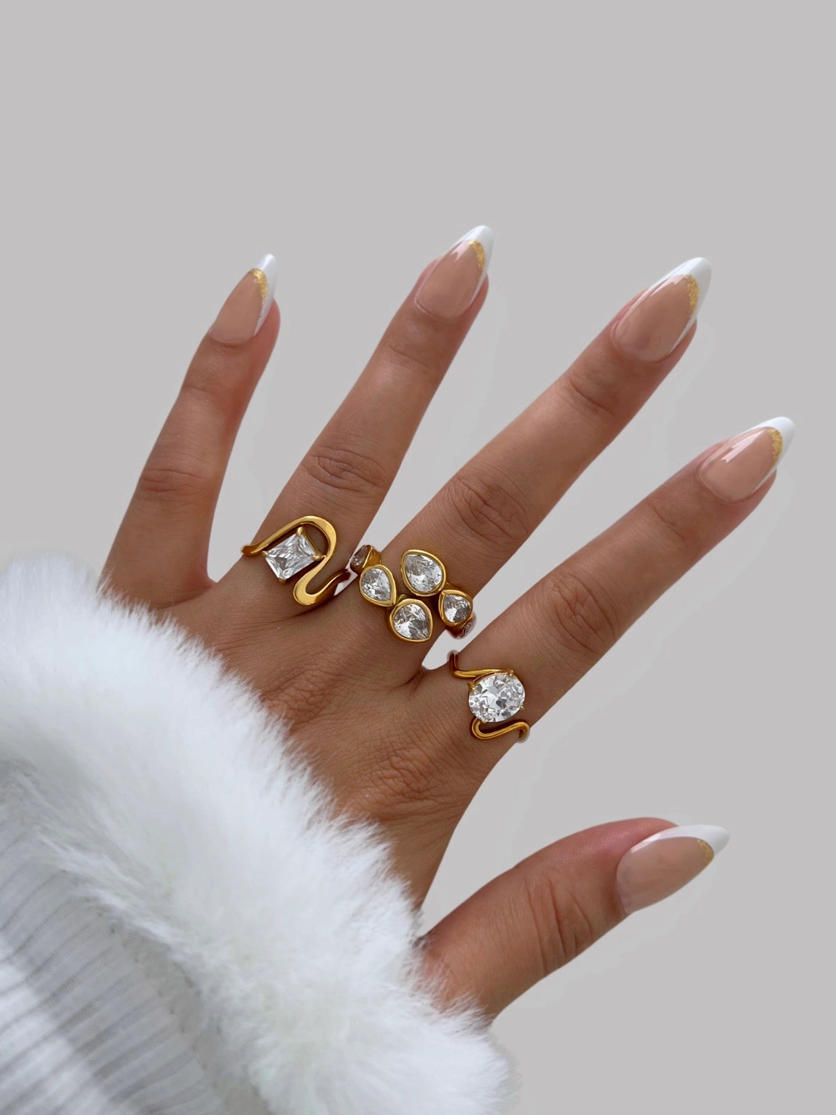 Lucie Rings – Worn on Finger-Hand wearing gold rings with clear stones on a neutral background