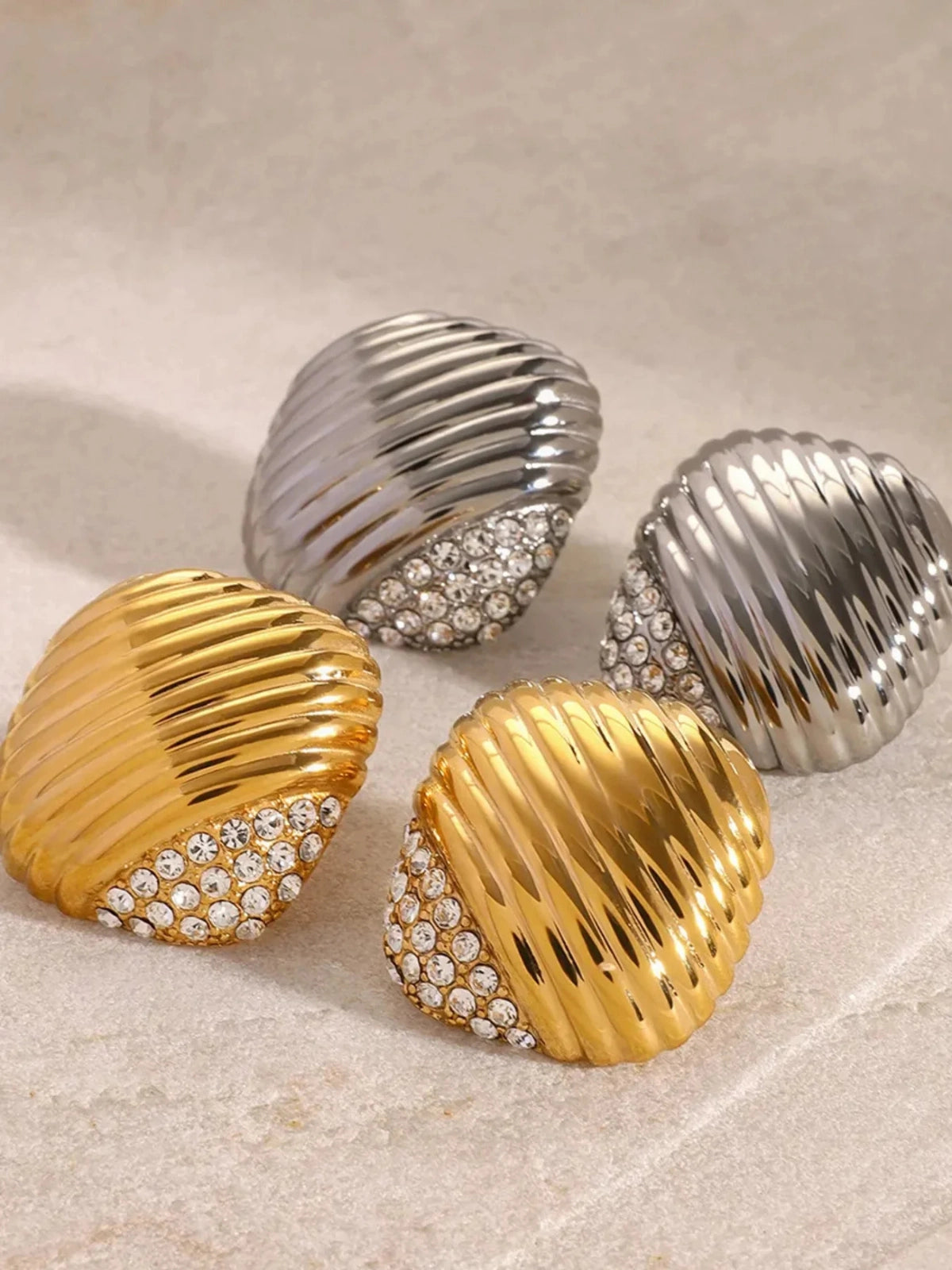 Natasha Earring – Close‑Up Detail- Pair of shell-shaped earrings in gold and silver on a textured surface