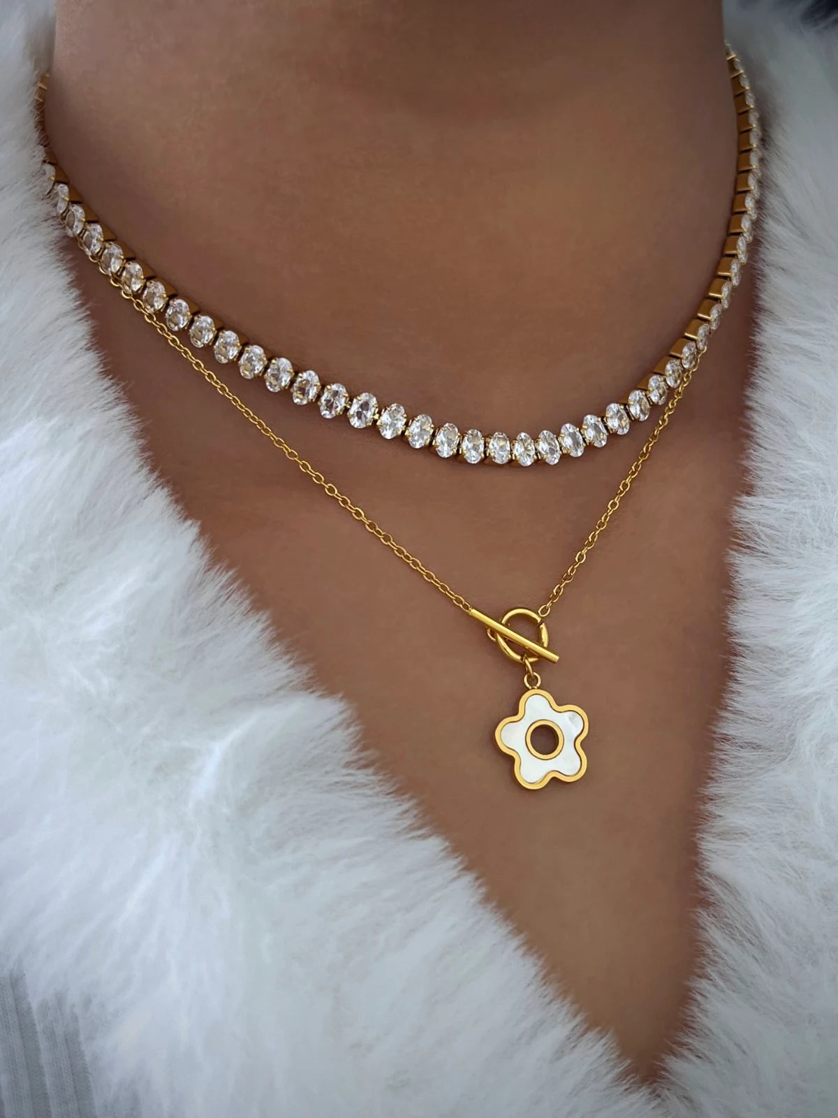 Noor Bracelet worn on neck — gold-plated stainless necklace by Shine With Me, elegant sizing 15.5 cm + 6 cm and subtle shimmer. Two gold necklaces with floral pendants on a white fur background