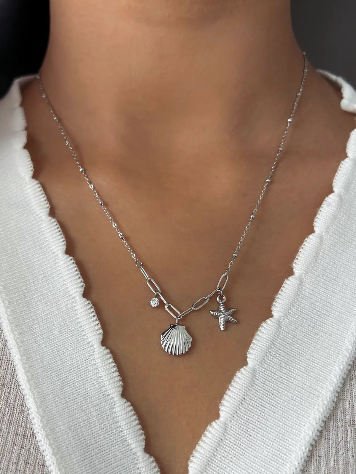 Nova Shell Necklace – On Model Styled Shot-Silver necklace with shell and starfish charms worn by a person in a white outfit.