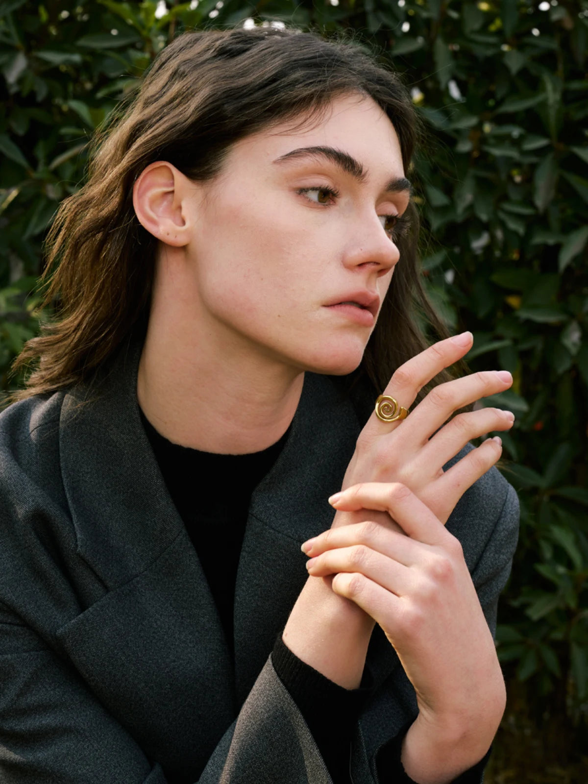 Ophelia Ring – Lifestyle / Everyday Look-Person wearing a dark coat with a blurred green leafy background
