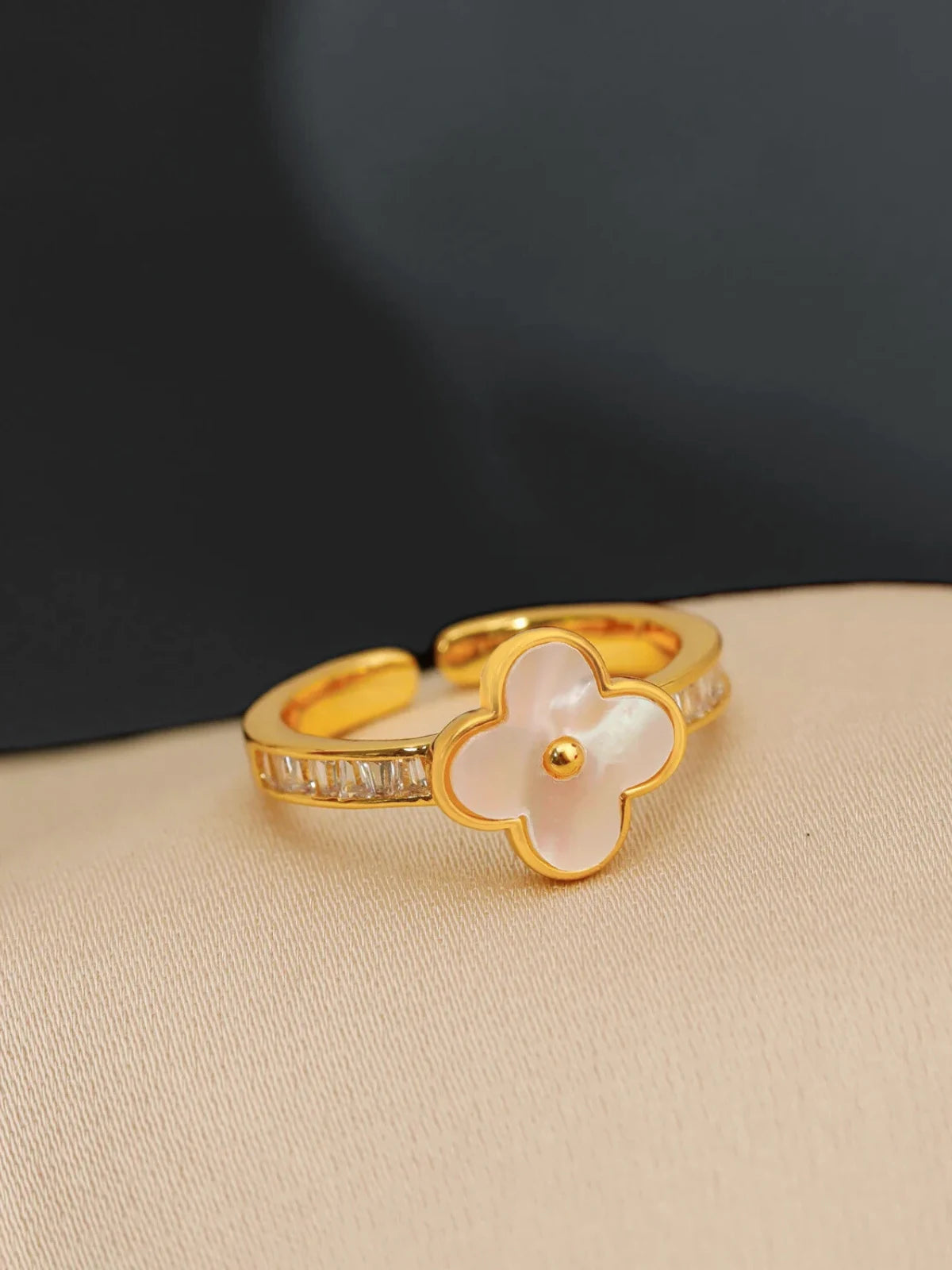 Pearl Bloom Ring – Close-Up Detail-Gold ring with a white flower design on a beige surface