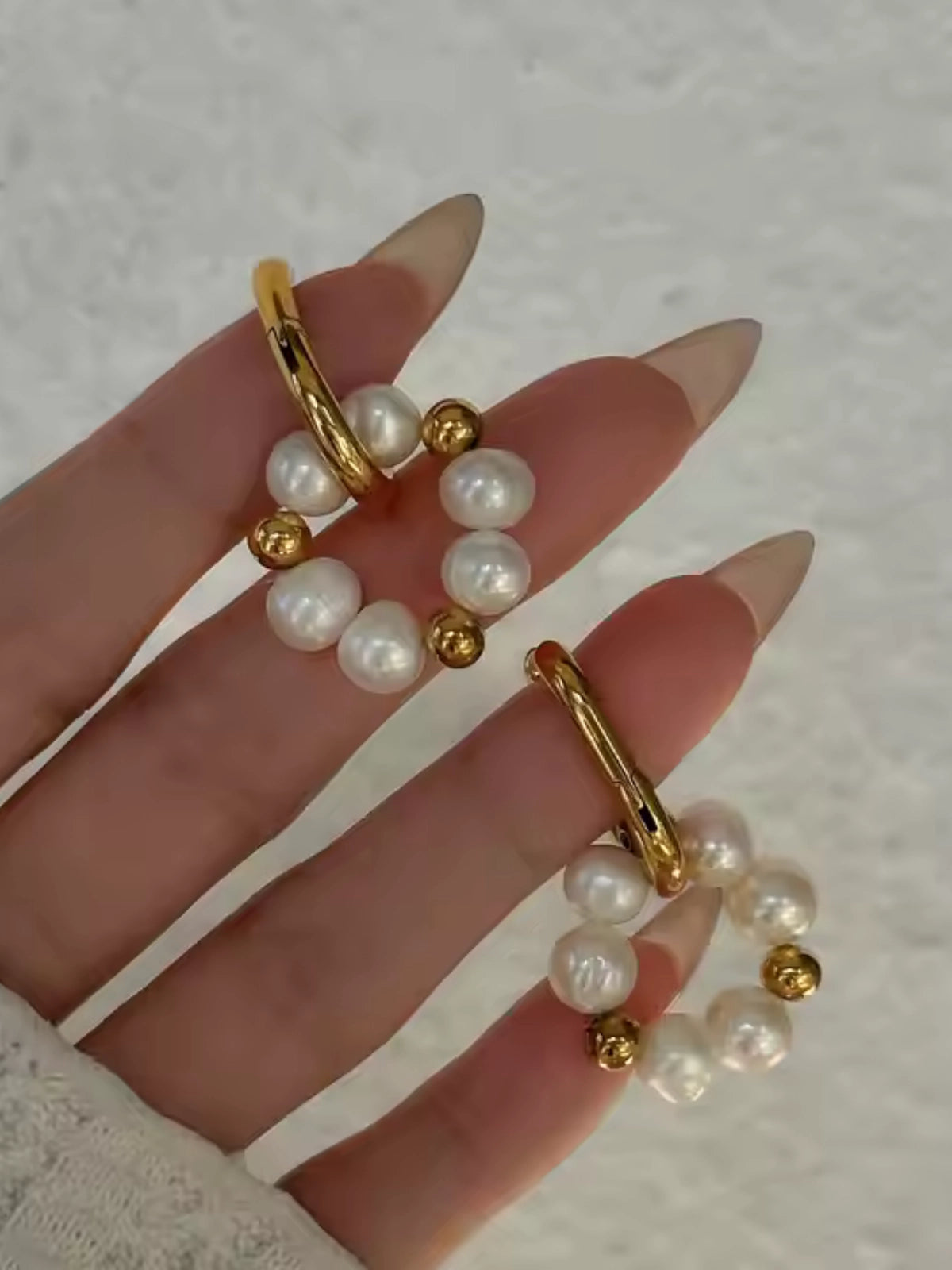Pearl Dream Hoop – Close‑Up Detail-Gold hoop earrings with pearl beads on a hand against a neutral background