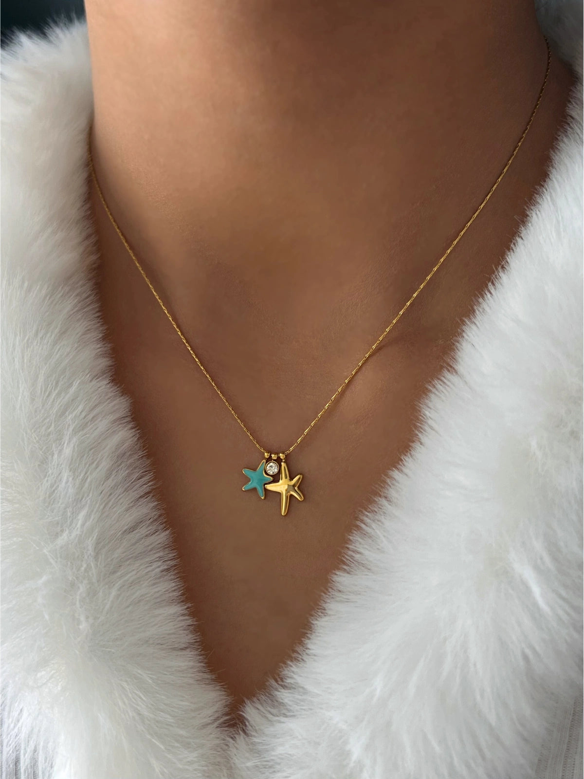 Seabell Necklace – On Model Styled Shot
-Necklace with star-shaped pendants on a person wearing a white fur garment.