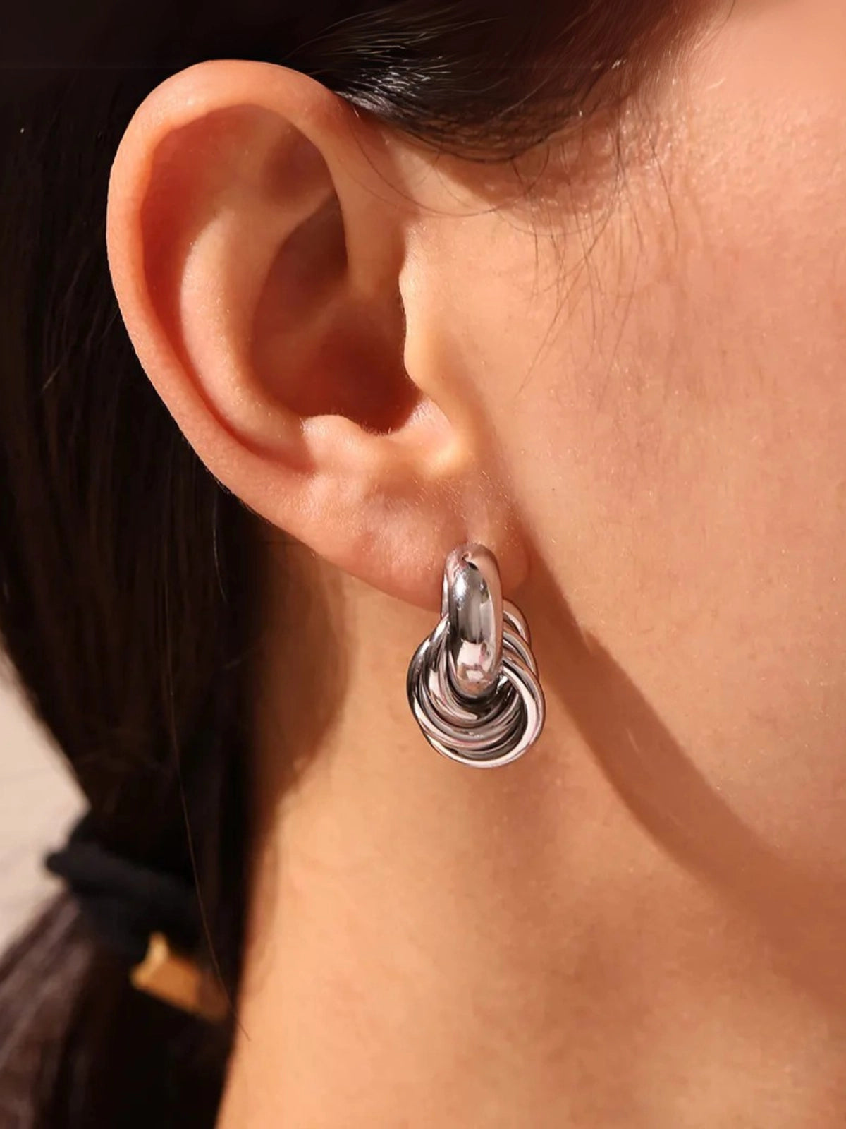 Close-up of Seabryn Earring by Shine With Me showing gold-plated finish, stainless steel base and craftsmanship for approx. 11 g weight. Close-up of an ear wearing a silver hoop earring with a blurred background
