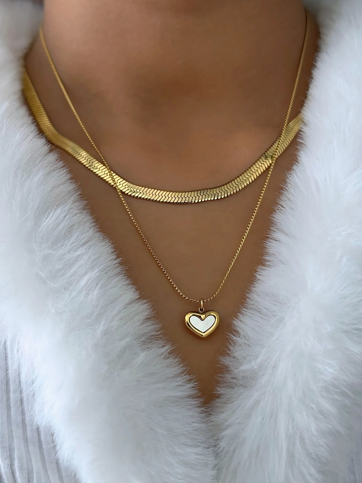 Slinka Chain – On Model Styled Shot-Gold necklaces with a heart pendant on a white fur background