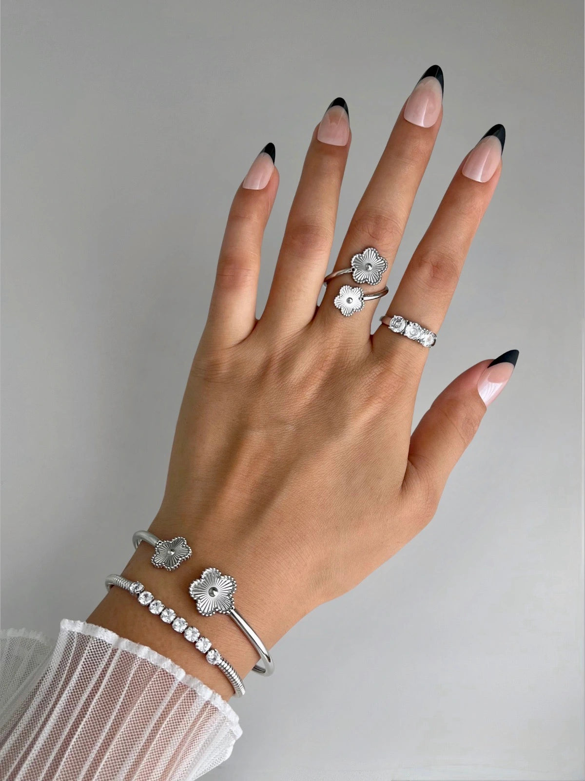 Sunveil Bangle Hand wearing silver rings and bracelets with black nail tips on a neutral background