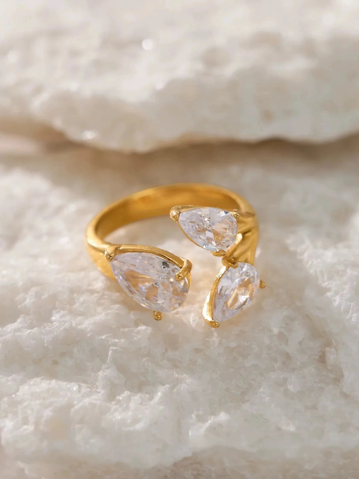 The Astria Ring – Close-Up Detail-Gold ring with pear-shaped diamonds on a textured white surface