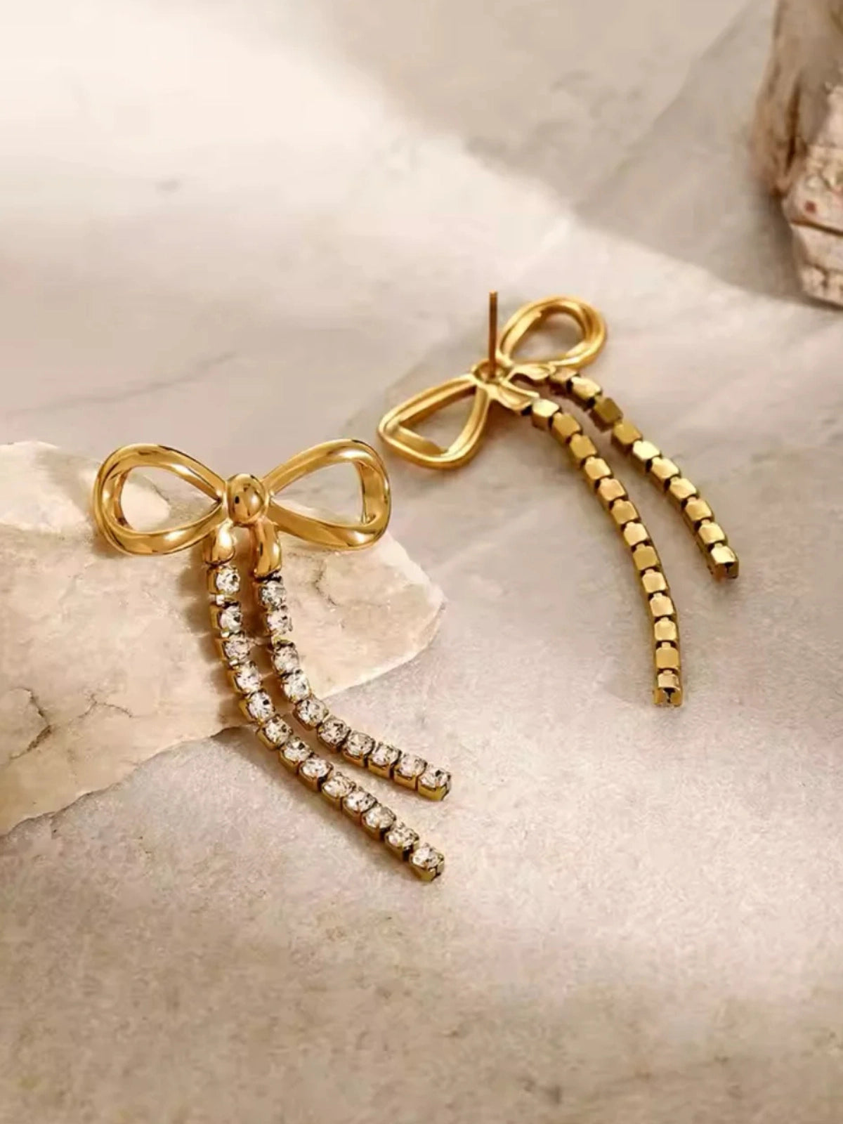 Valentina Bow Earring – On Ear / Styled Shot, Gold bow-shaped earrings with rhinestone details on a marble surface
