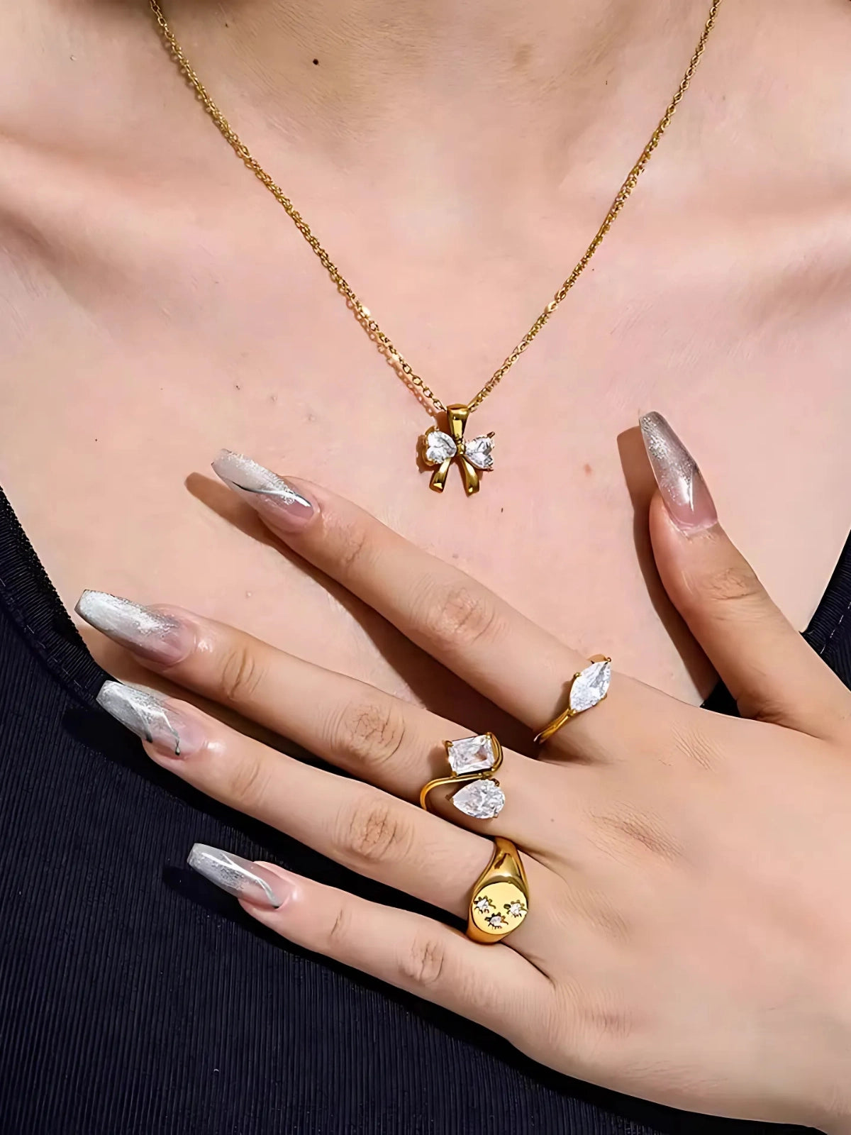 Water Drop Ring – Close-up of a person wearing gold jewelry including a necklace, rings, and a bow-shaped pendant.