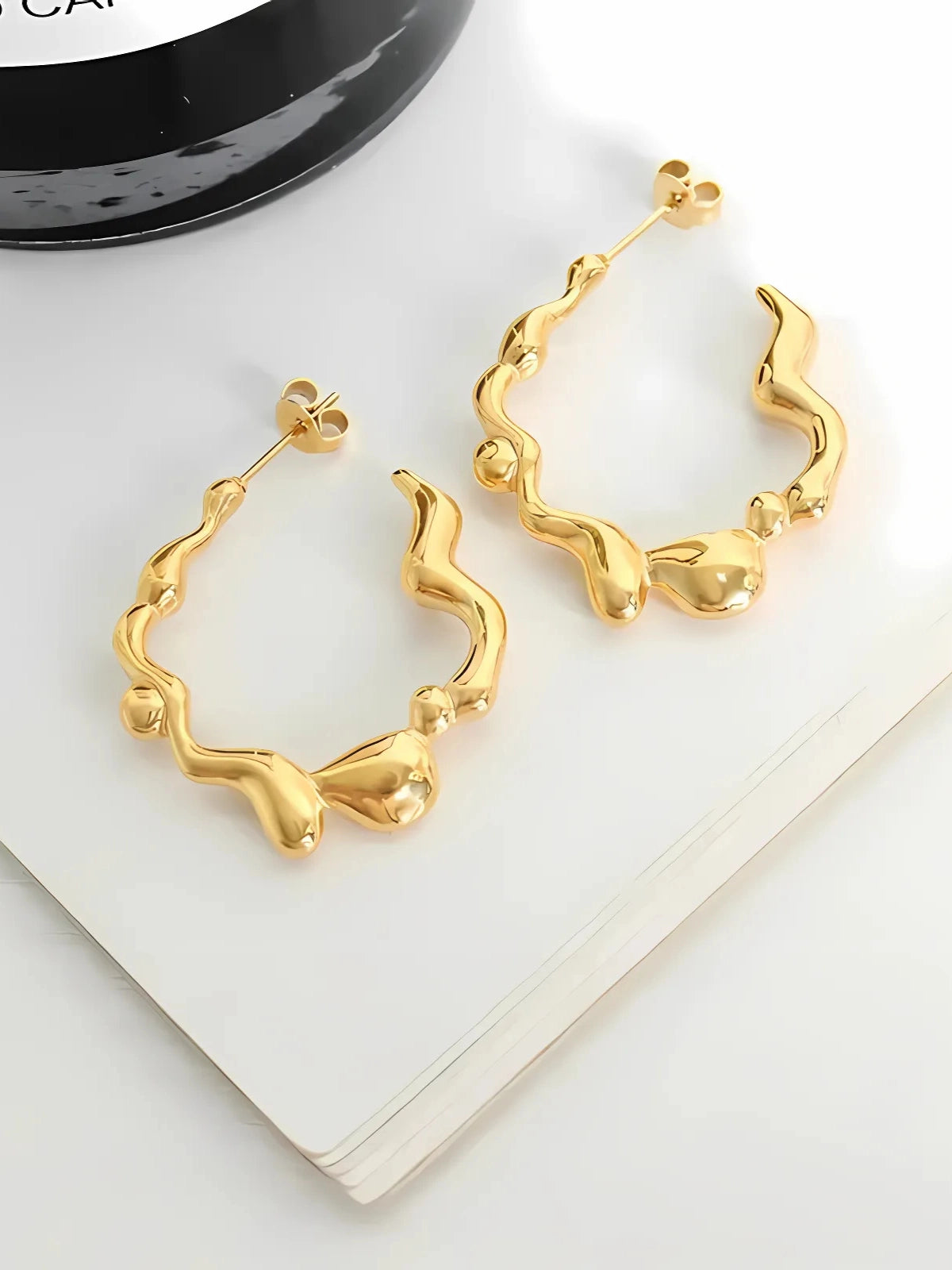 Zelina Earrings – Close‑Up Detail-Gold hoop earrings on a white surface