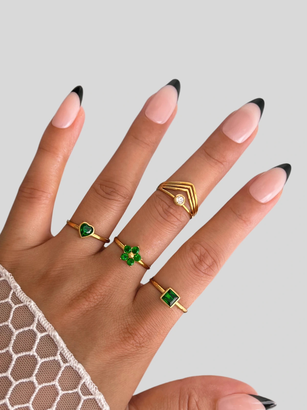 dua-ring-closeup-detail-shine-with-me-Hand wearing gold rings with green gemstones on a neutral background