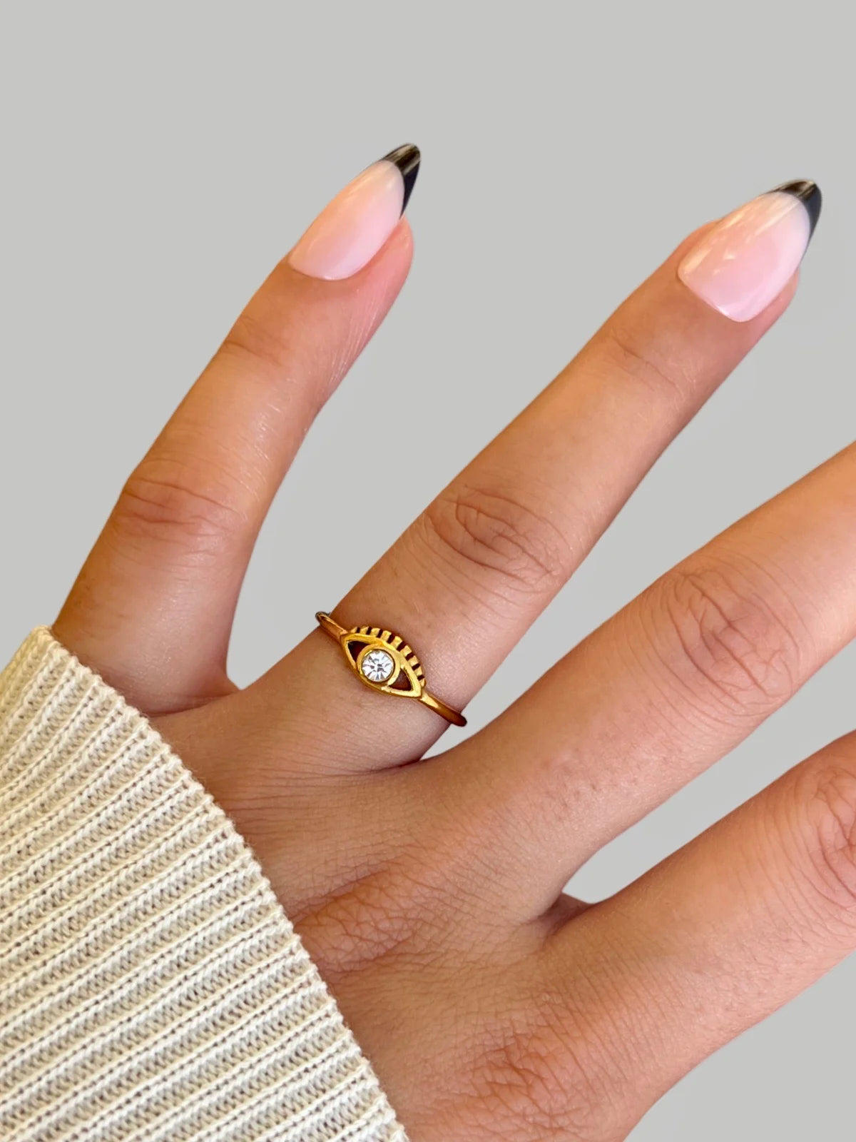 golden-eye-charm-ring-lifestyle-shot-shine-with-me Gold ring with a diamond on a finger against a gray background