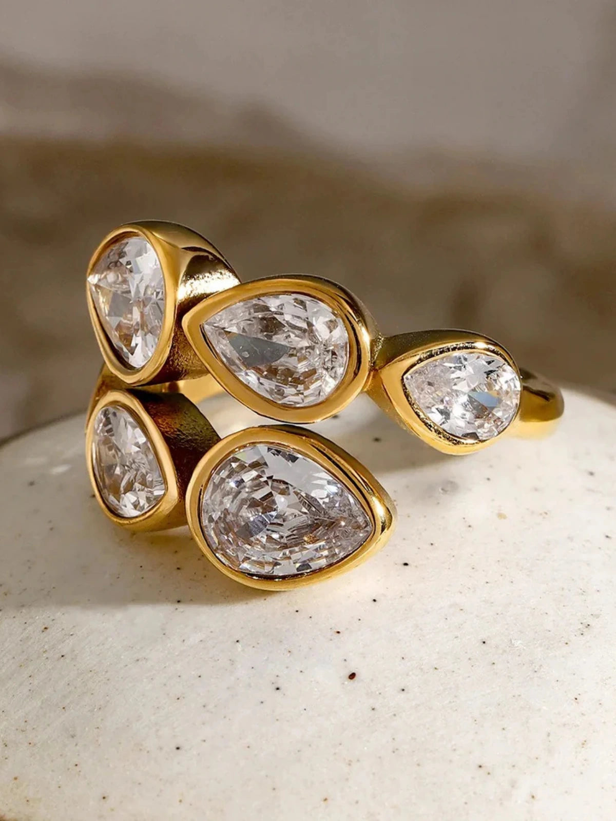 noa-ring-lifestyle-shot-shine-with-me Gold ring with pear-shaped diamonds on a textured surface