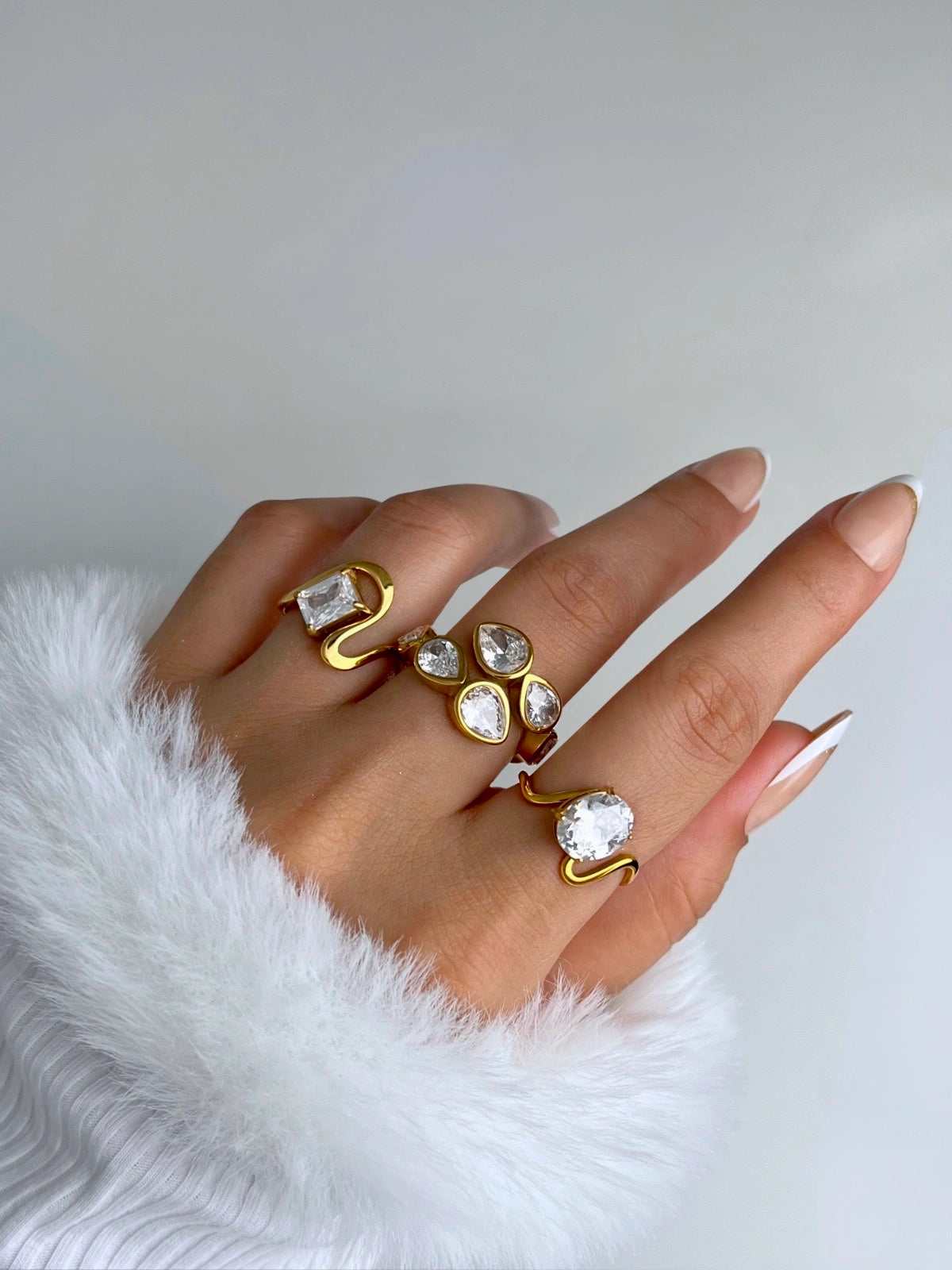 noa-ring-side-angle-shine-with-me-Hand wearing multiple gold and crystal rings on a white background
