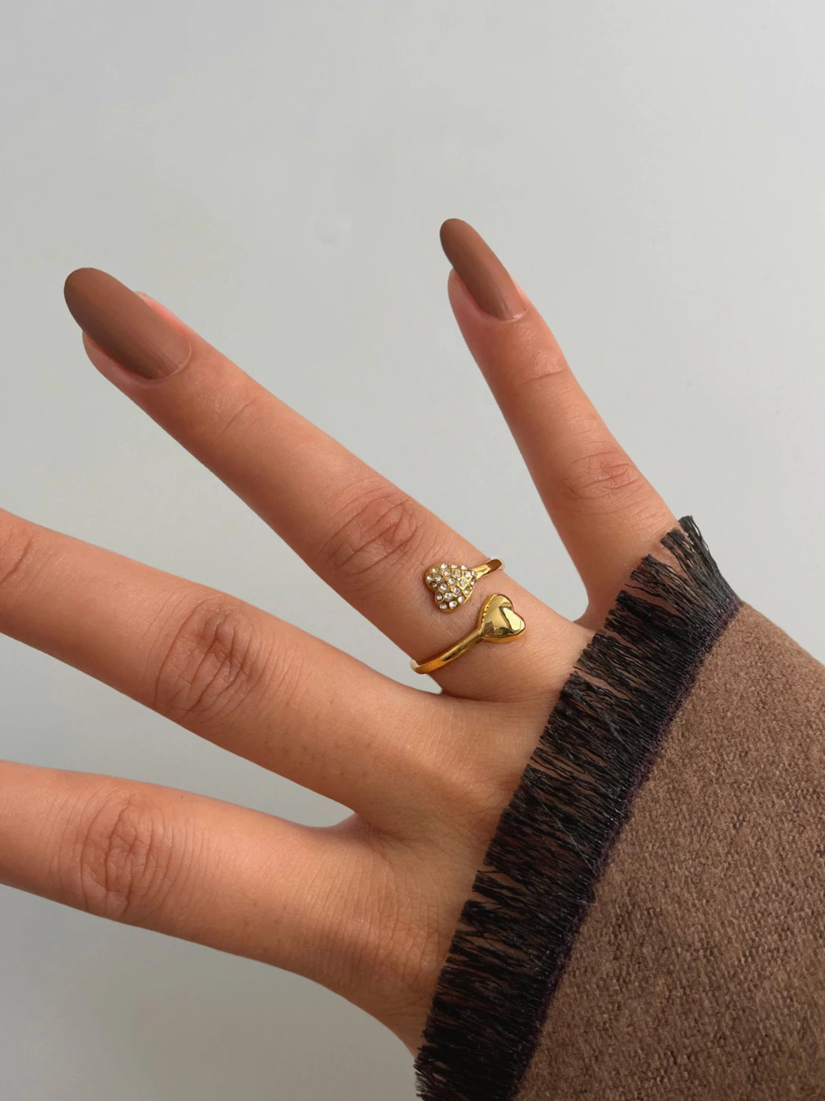 us-together-ring-side-angle-shine-with-me Hand wearing two gold rings on a plain background
