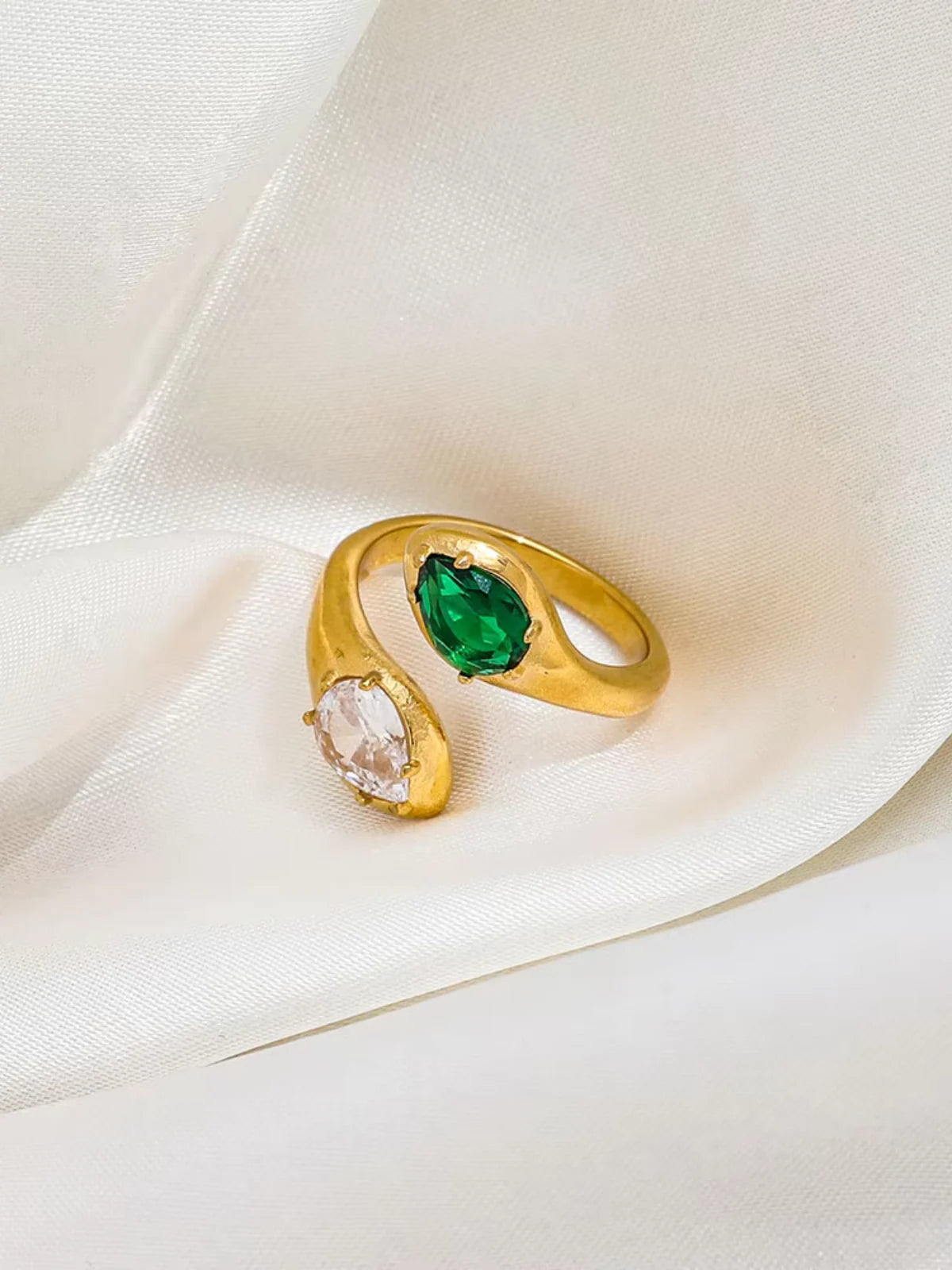 Alexandra_Ring_Front_View_1 Gold ring with green and clear gemstones on a white fabric background