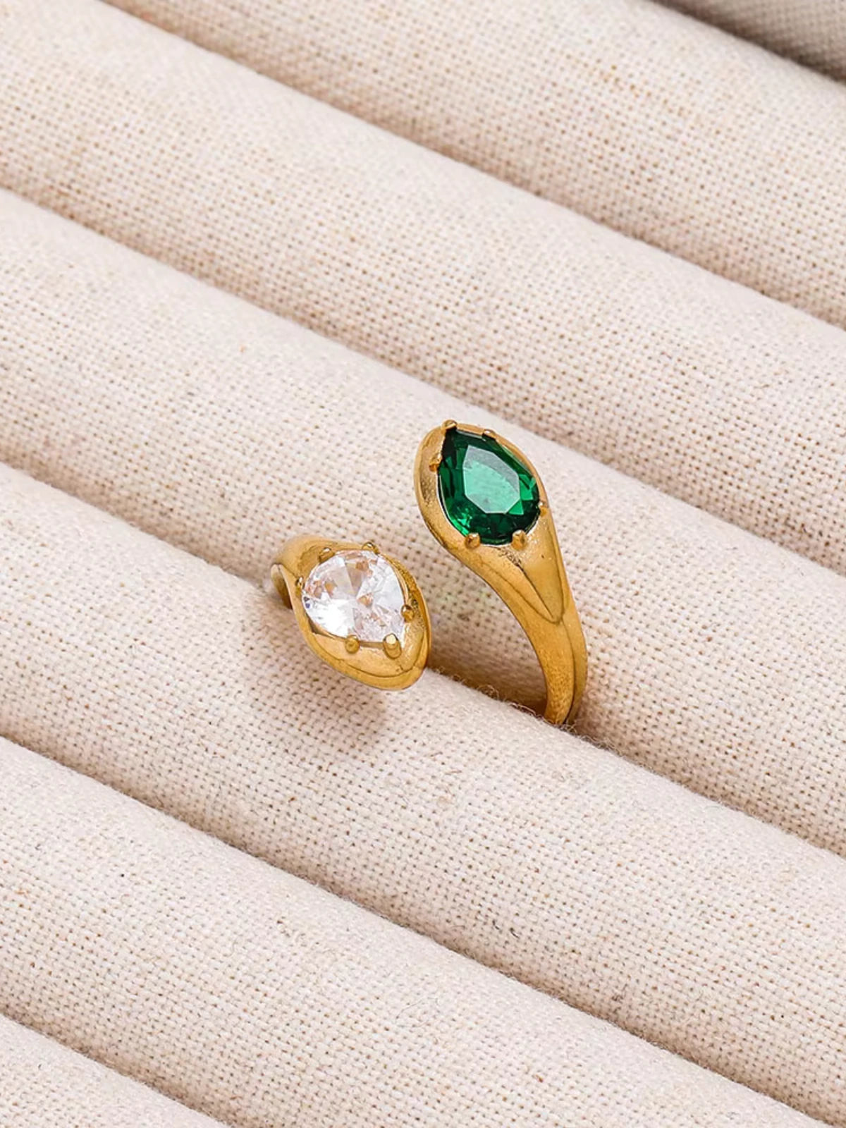 Alexandra_Ring_Front_View_2 Gold ring with green gemstone and clear stone on beige fabric