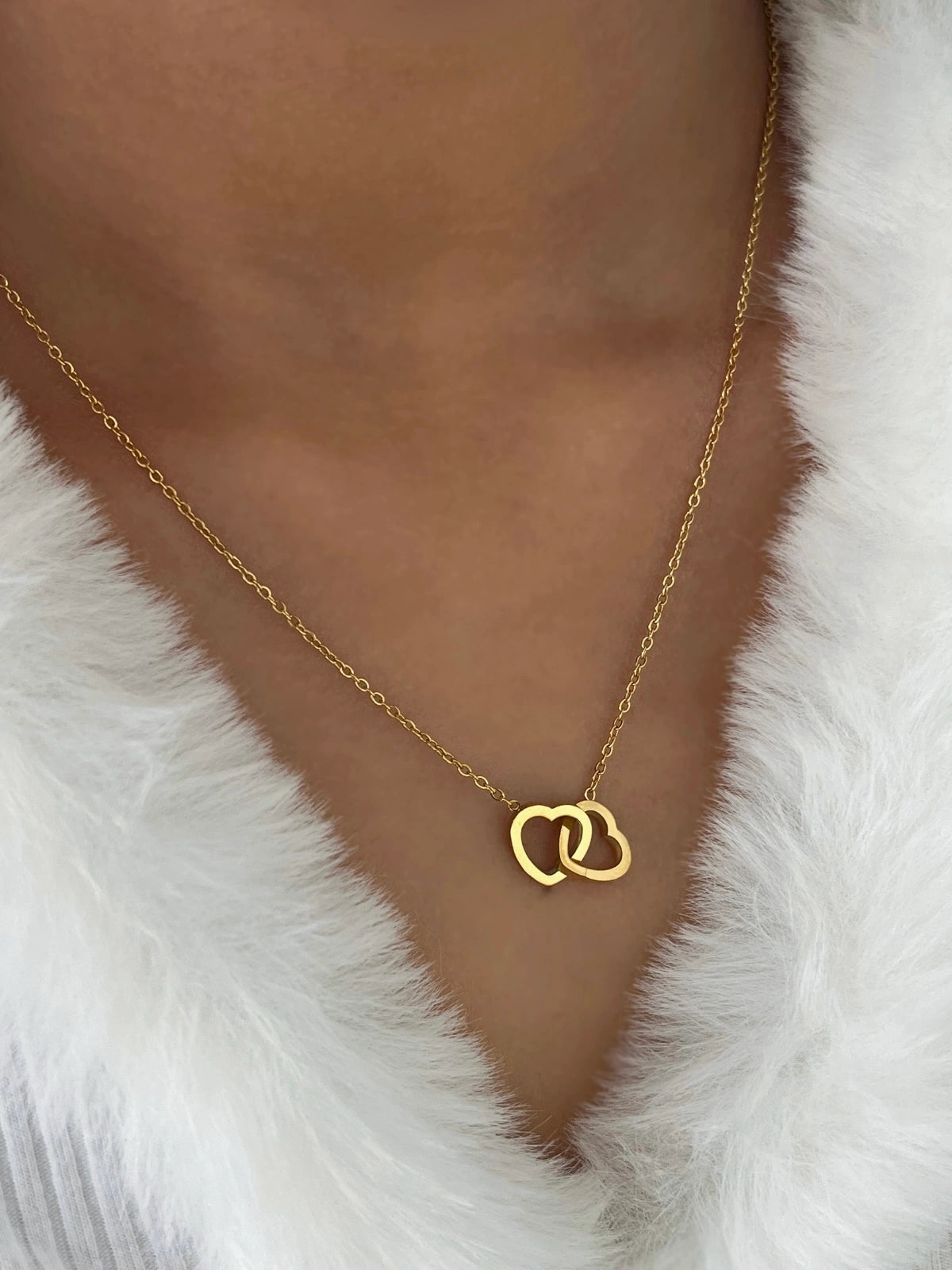 All My Love Necklace – On Model Styled Shot-Gold necklace with a heart pendant on a person wearing a white fur garment.