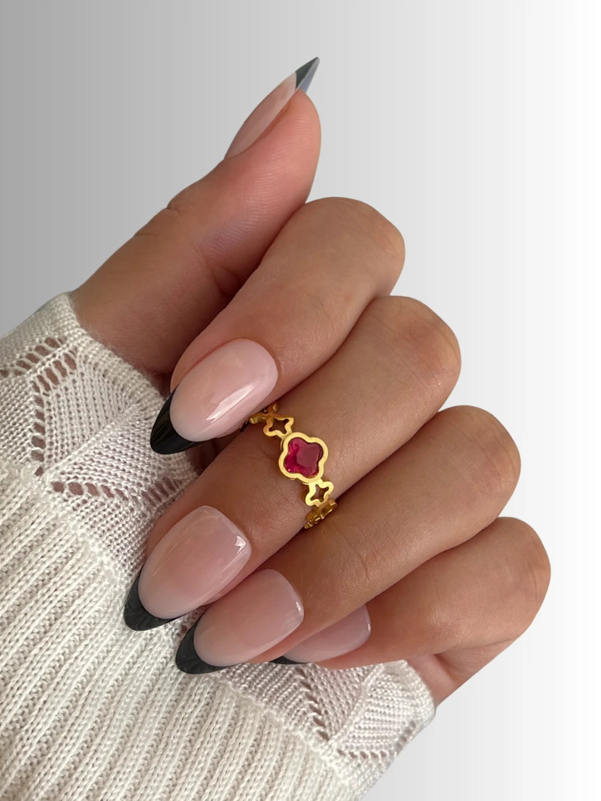Amara Clover Ring | Shine With Me Hand with a gold ring featuring a red gemstone on a white background