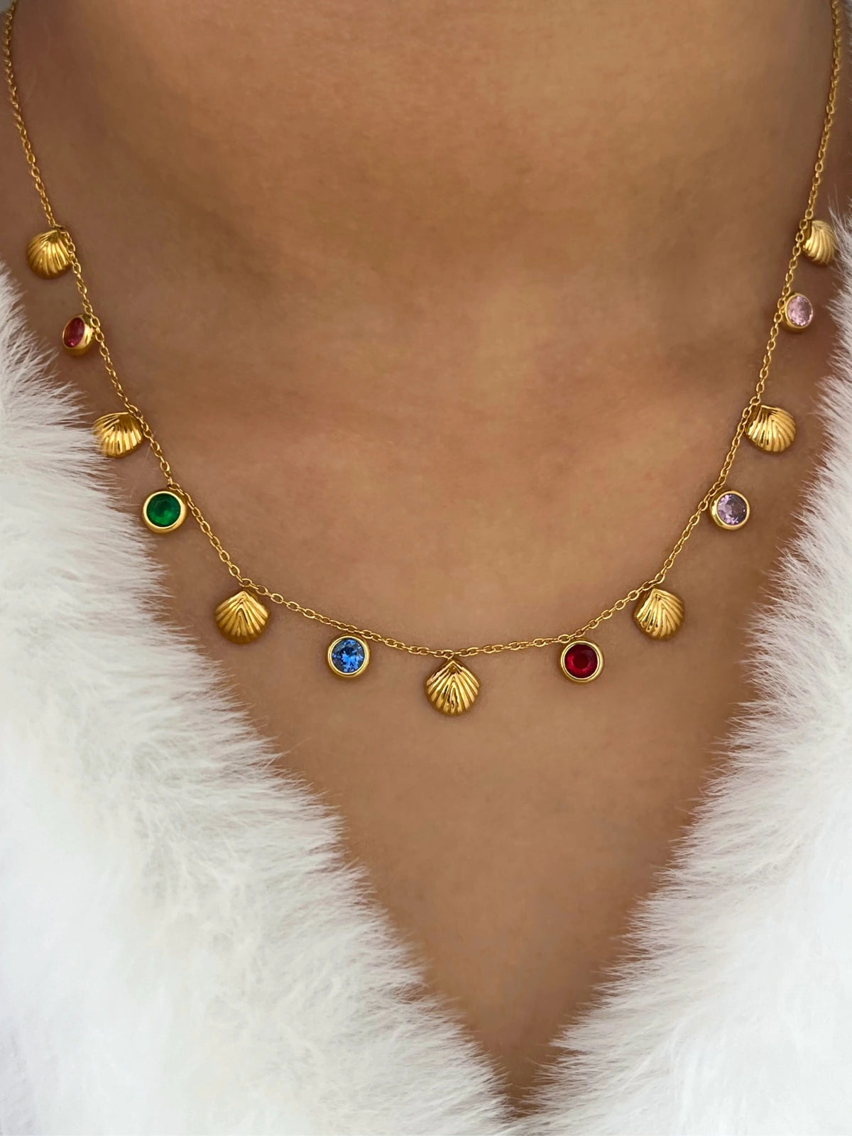 Bella Necklace – On Model Styled Shot-Gold necklace with colorful gemstones on a person wearing a white fur coat.