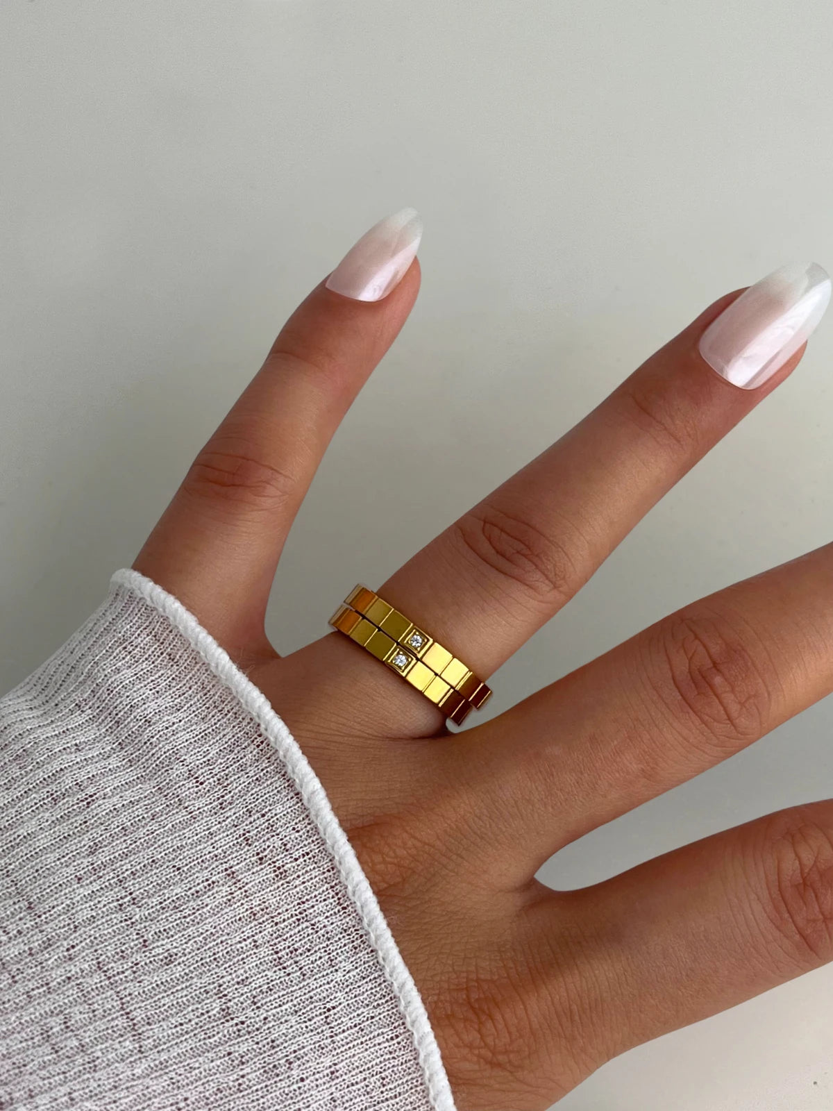 Celina RING Hand wearing a gold ring with a textured band on a neutral background