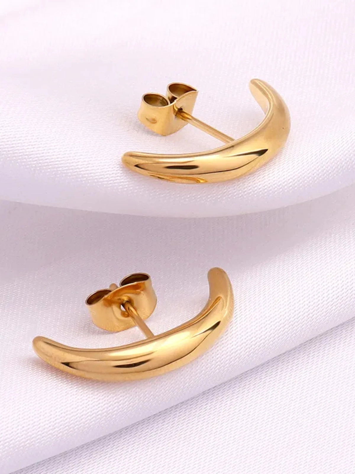 Celora Earring – Close‑Up Detail-1- Gold crescent-shaped earrings on a white fabric background