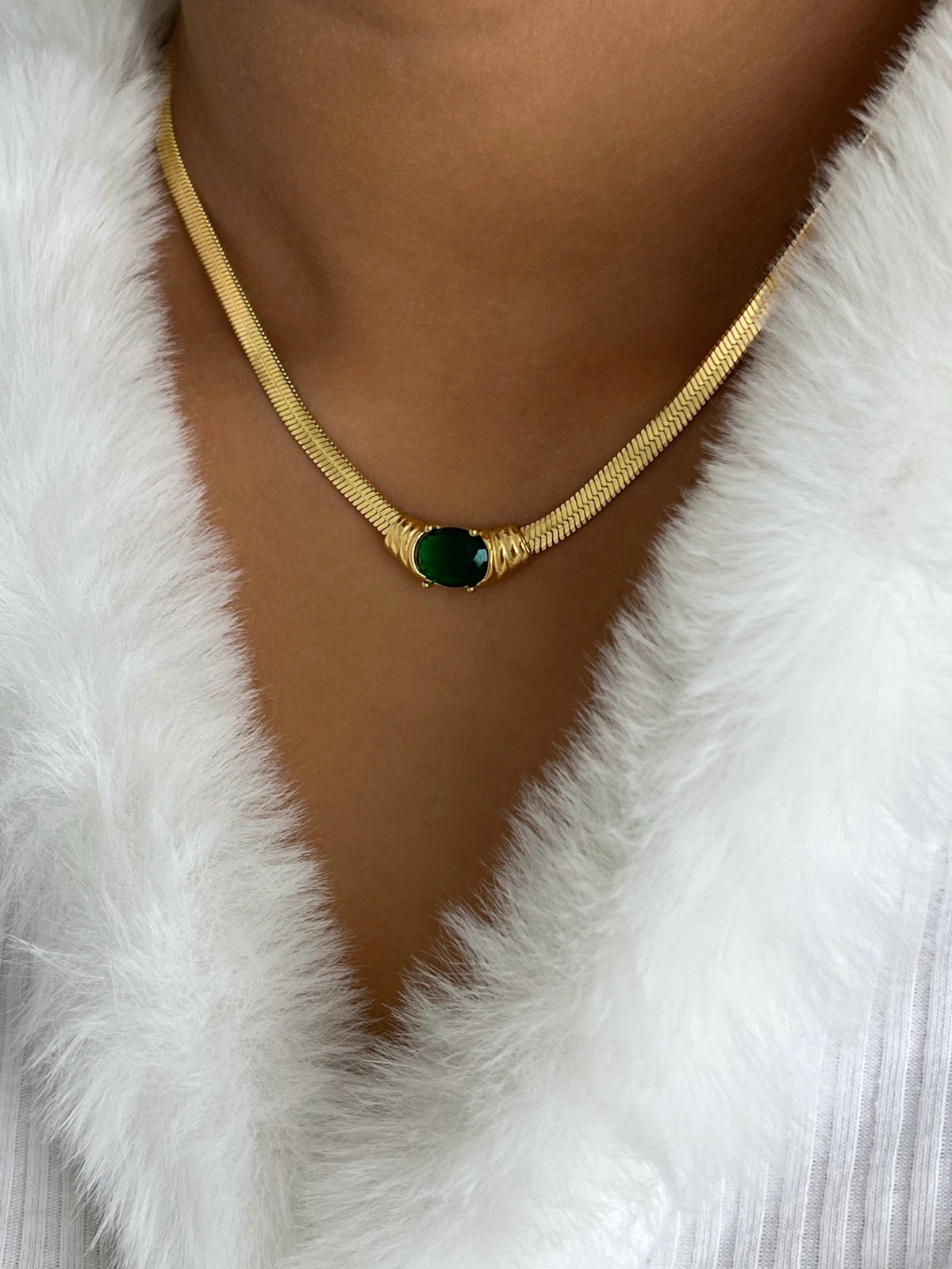 Chanel Necklace worn around neck — 18K gold-plated stainless steel with cubic zirconia by Shine With Me, chain length 41 cm + 6 cm extender.-Gold necklace with a green pendant on a person wearing a white fur garment.
