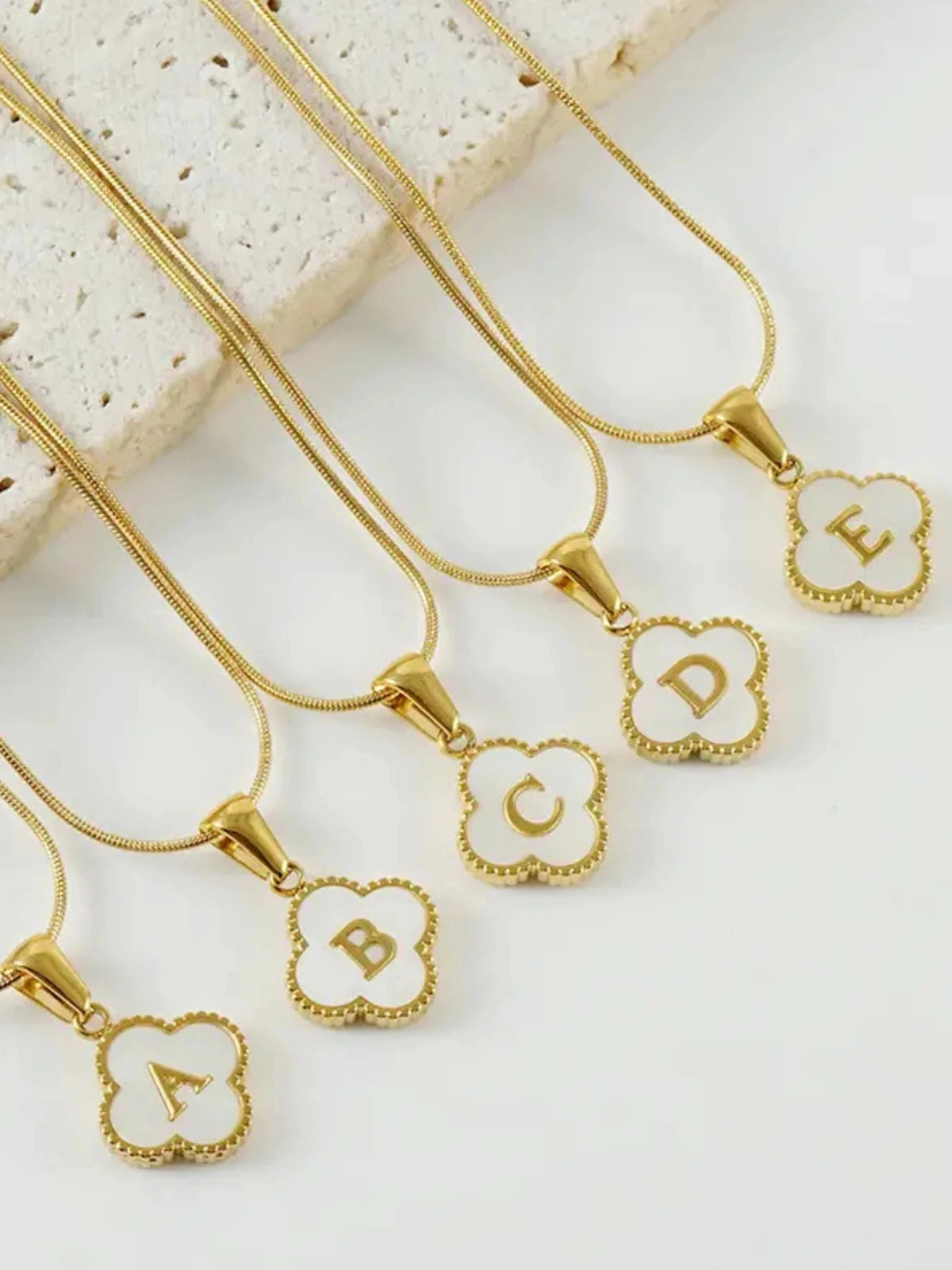 Clover Letter Necklace – Close‑Up Detail-Gold necklaces with letter charms on a light background