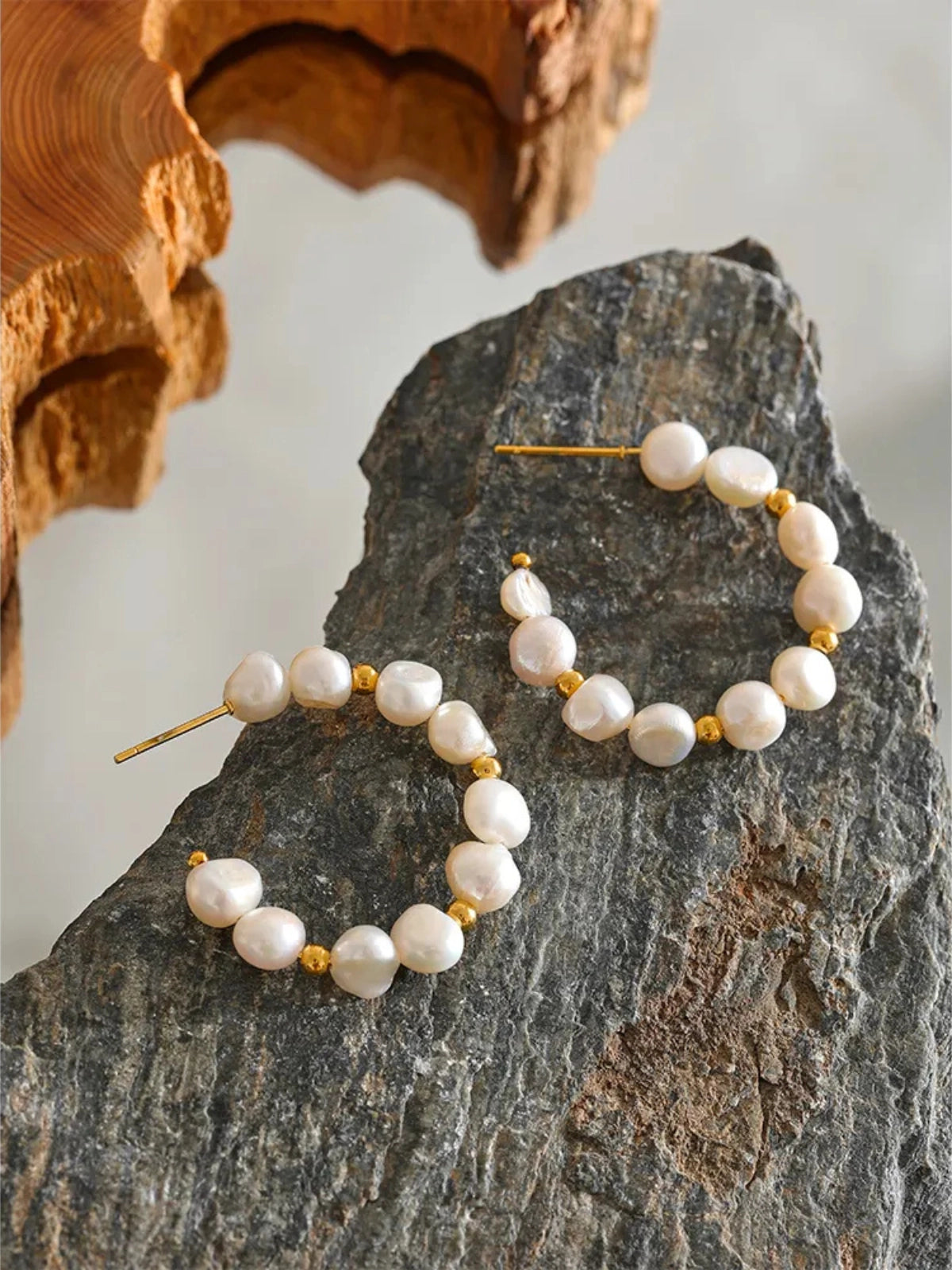 Close‑up of Cyndi Pearl Hoop Earring by Shine With Me showing gold‑plated finish, hoop design and freshwater pearl accent-Pearl hoop earrings on a stone surface with a natural background
