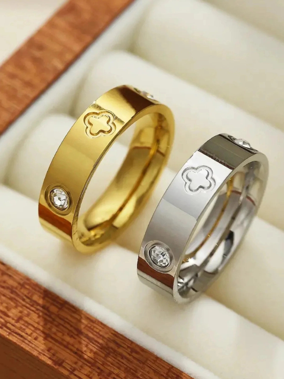 Dawn Ring – Lifestyle / Everyday Look-Gold and silver rings with clover designs and small diamonds on a wooden surface.