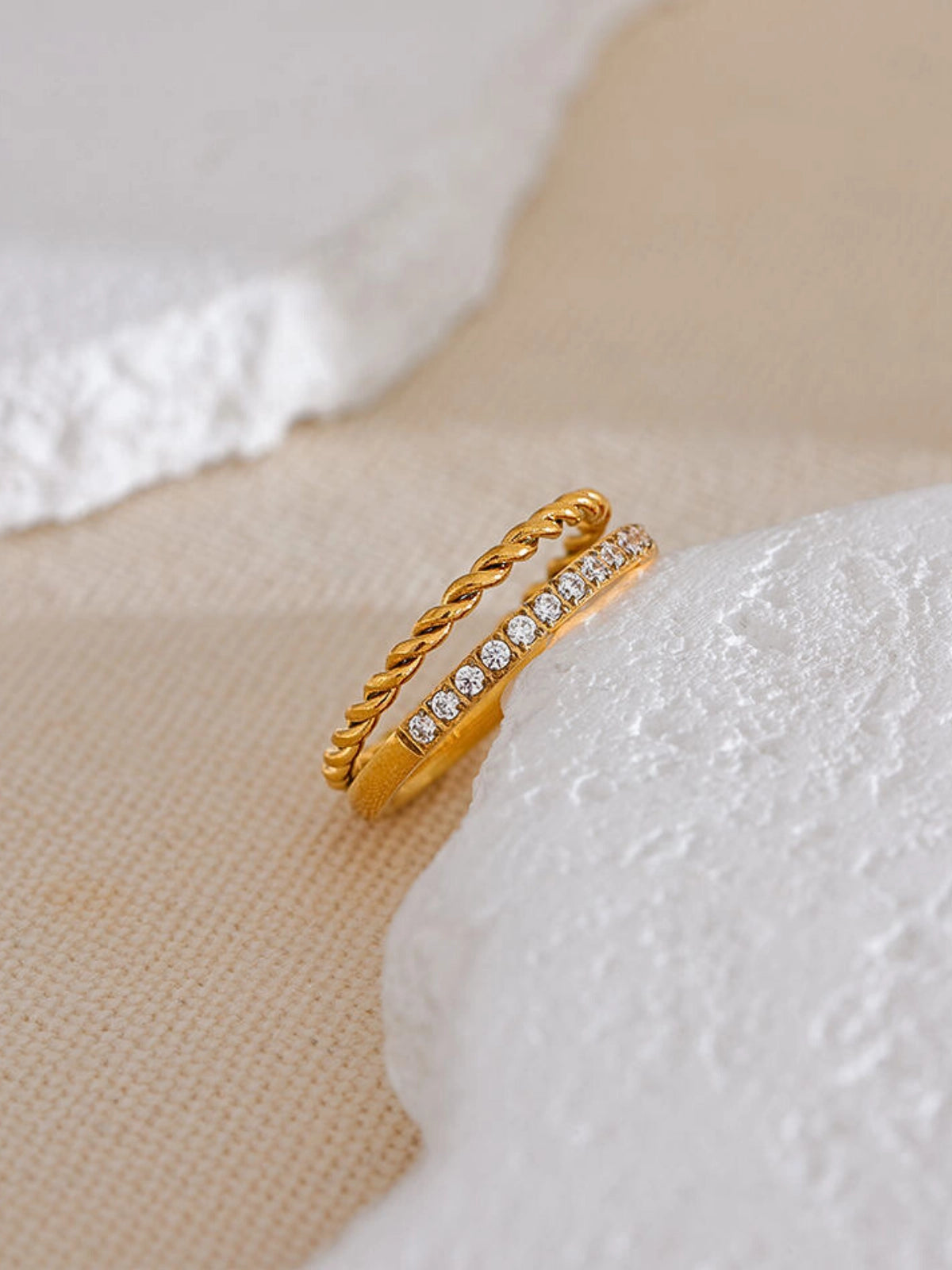 Elegance_Ring_Front_View_1. Gold ring with diamond accents on a textured beige surface