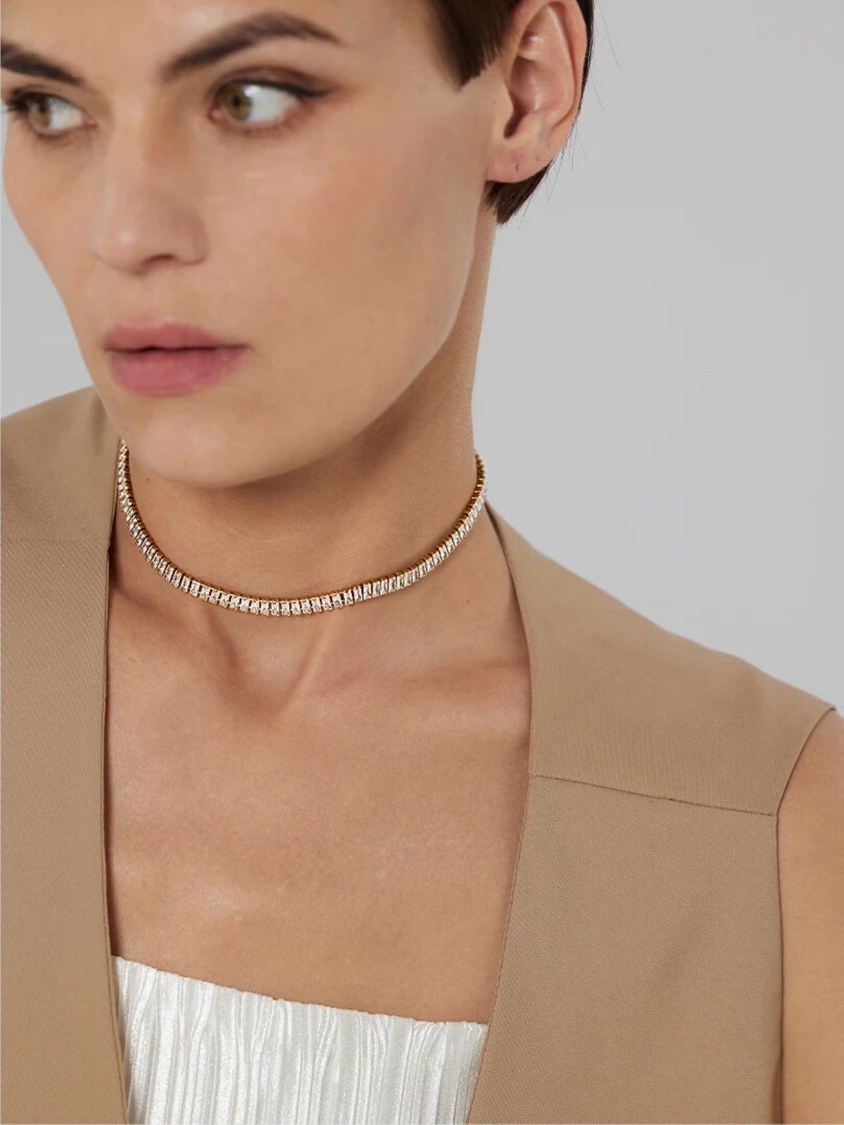 Elly_Chain Woman wearing a gold necklace against a neutral background