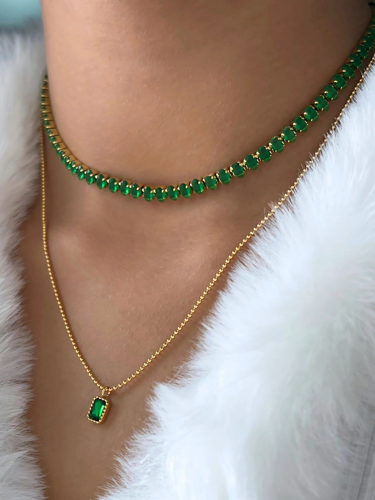 Emily Chain – On Model Styled Shot-Gold necklace with green gemstones worn by a person against a white fur background