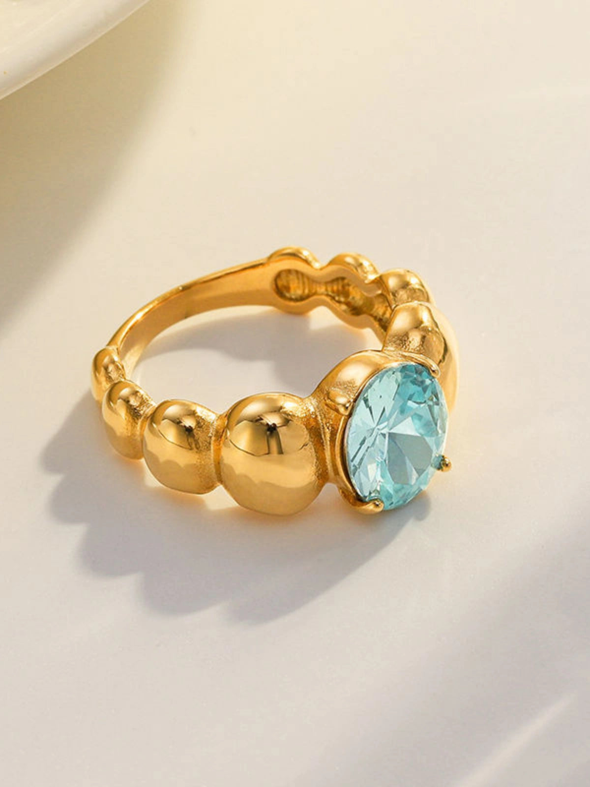 Fabiana_Ring_Front_View. Gold ring with a blue gemstone on a light background